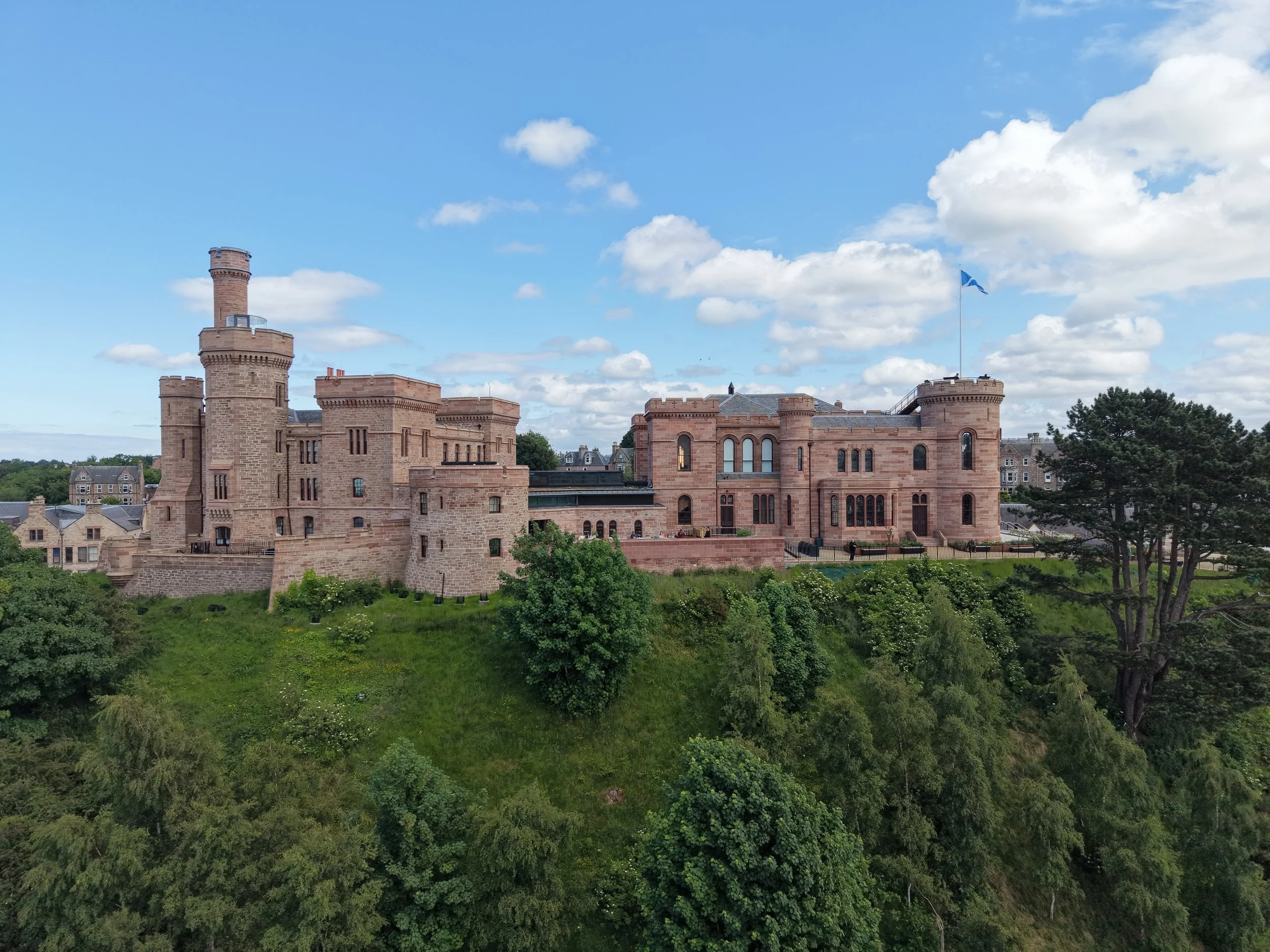 Perched high on a cliff overlooking the tranquil waters of the River Ness, Inverness Castle stands as a striking symbol of the capital of the Scottish Highlands. Built in the mid-19th century from distinctive red-pink sandstone, its symmetrical tower