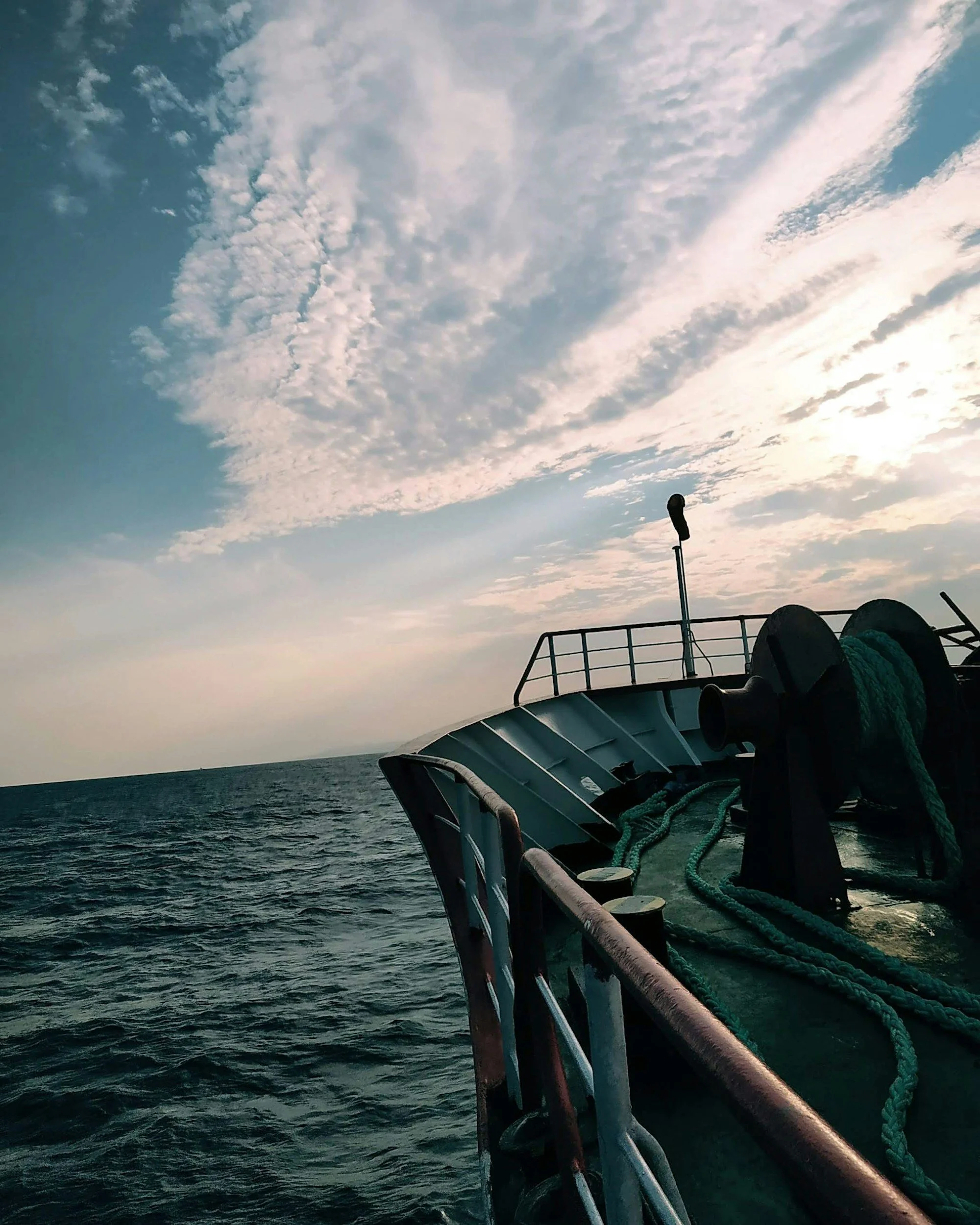 View from a boat showing a cloudy sky and the ocean, with parts of the boat's deck, railings, and ropes visible in the foreground.