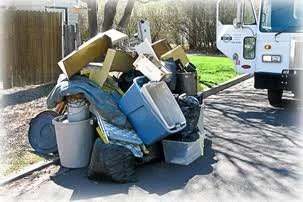 Pile of trash including boxes, a computer monitor, appliances, and other debris on the side of a street