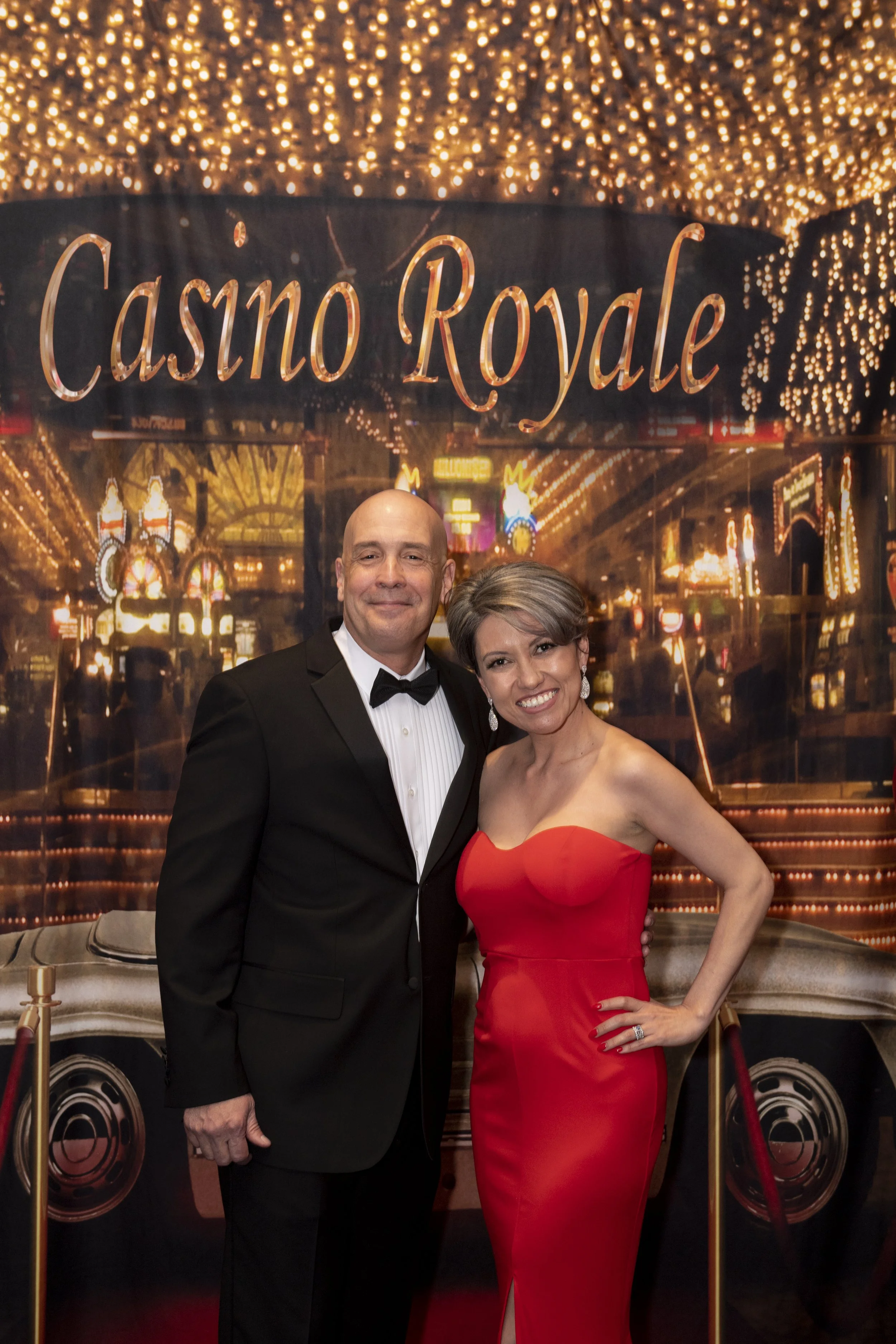 Rich and Amanda Rodriguez posing together at the Casino Royale backdrop with golden lights and a movie theme.
