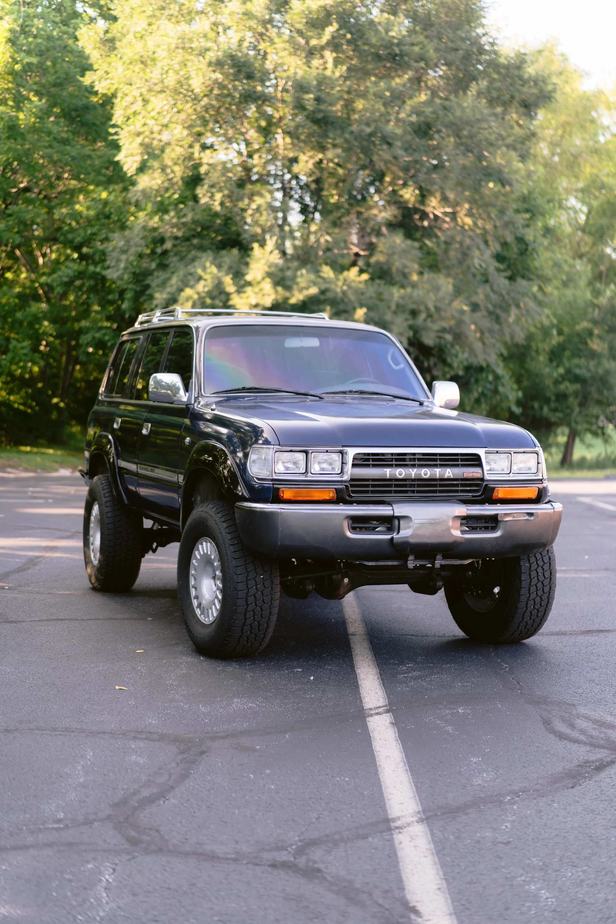 A black Toyota SUV parked in a parking lot on a sunny day with green trees in the background.