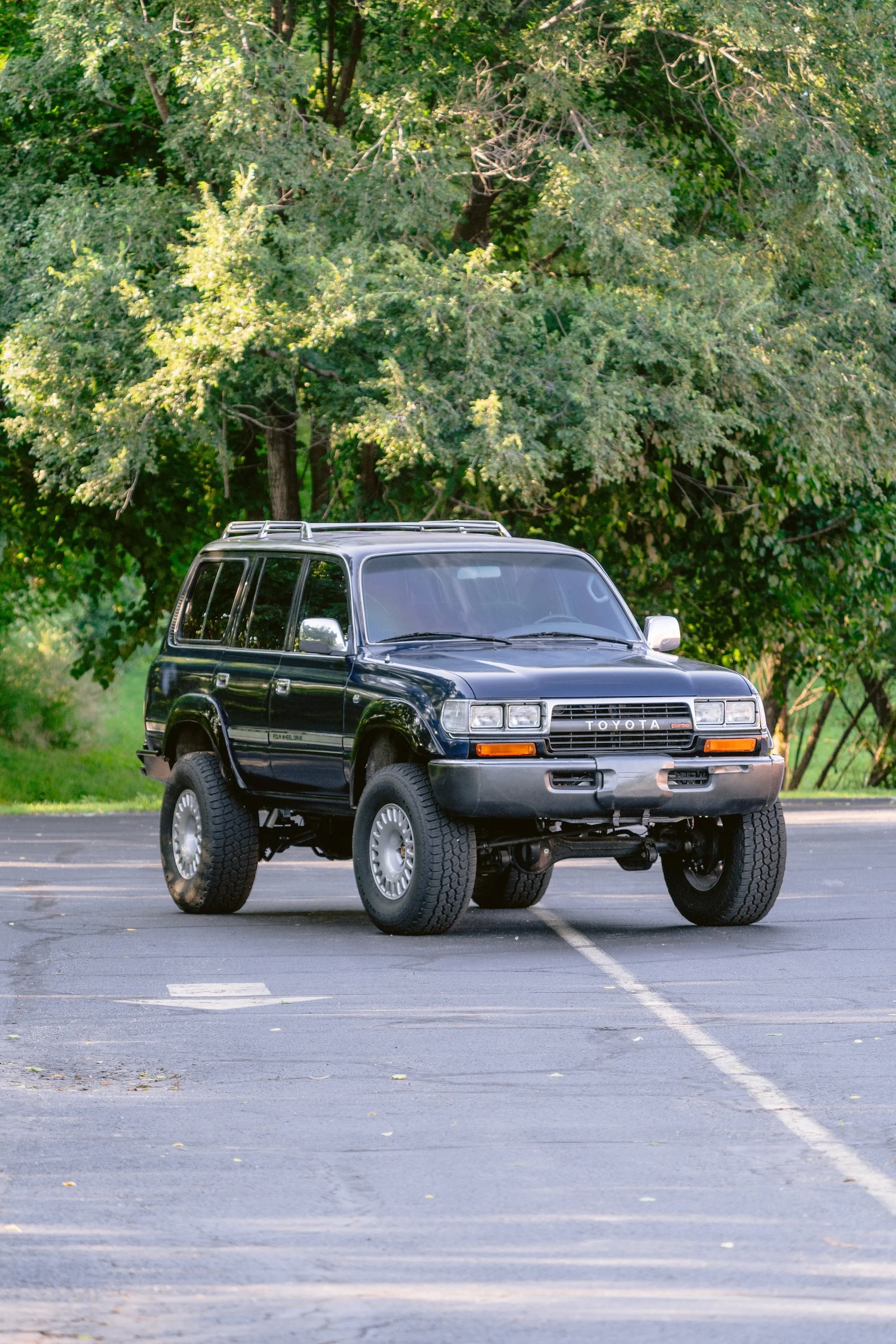 A black off-road Toyota SUV with large tires parked in an empty parking lot surrounded by green trees.