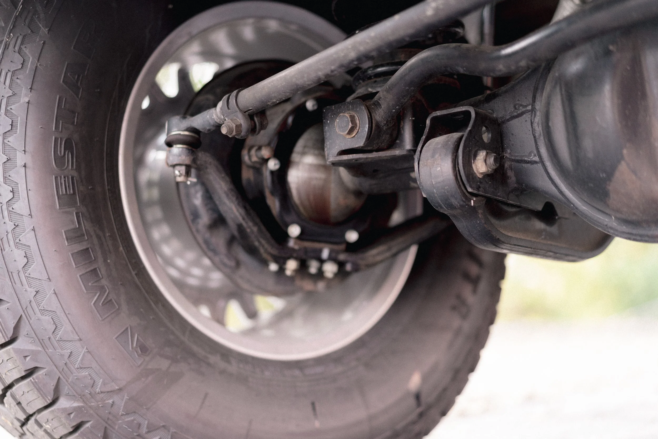 Close-up of a vehicle's wheel and suspension component, showing tire tread and metal parts of the suspension system.