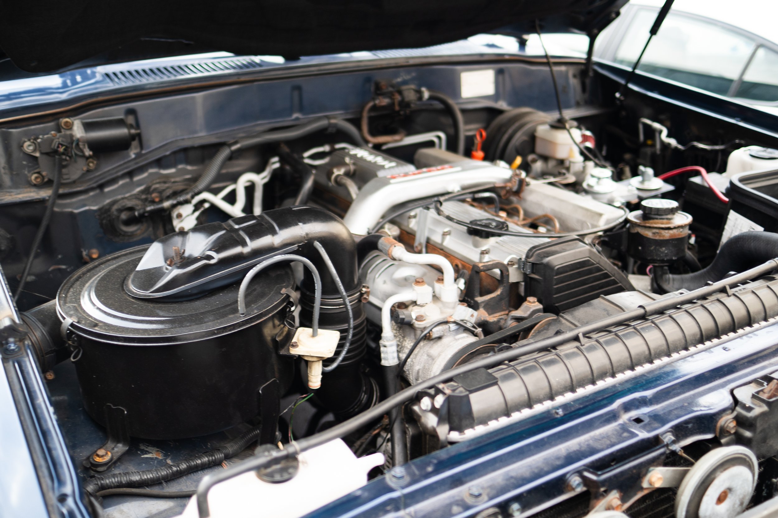 Car engine bay with various engine components, hoses, and wiring