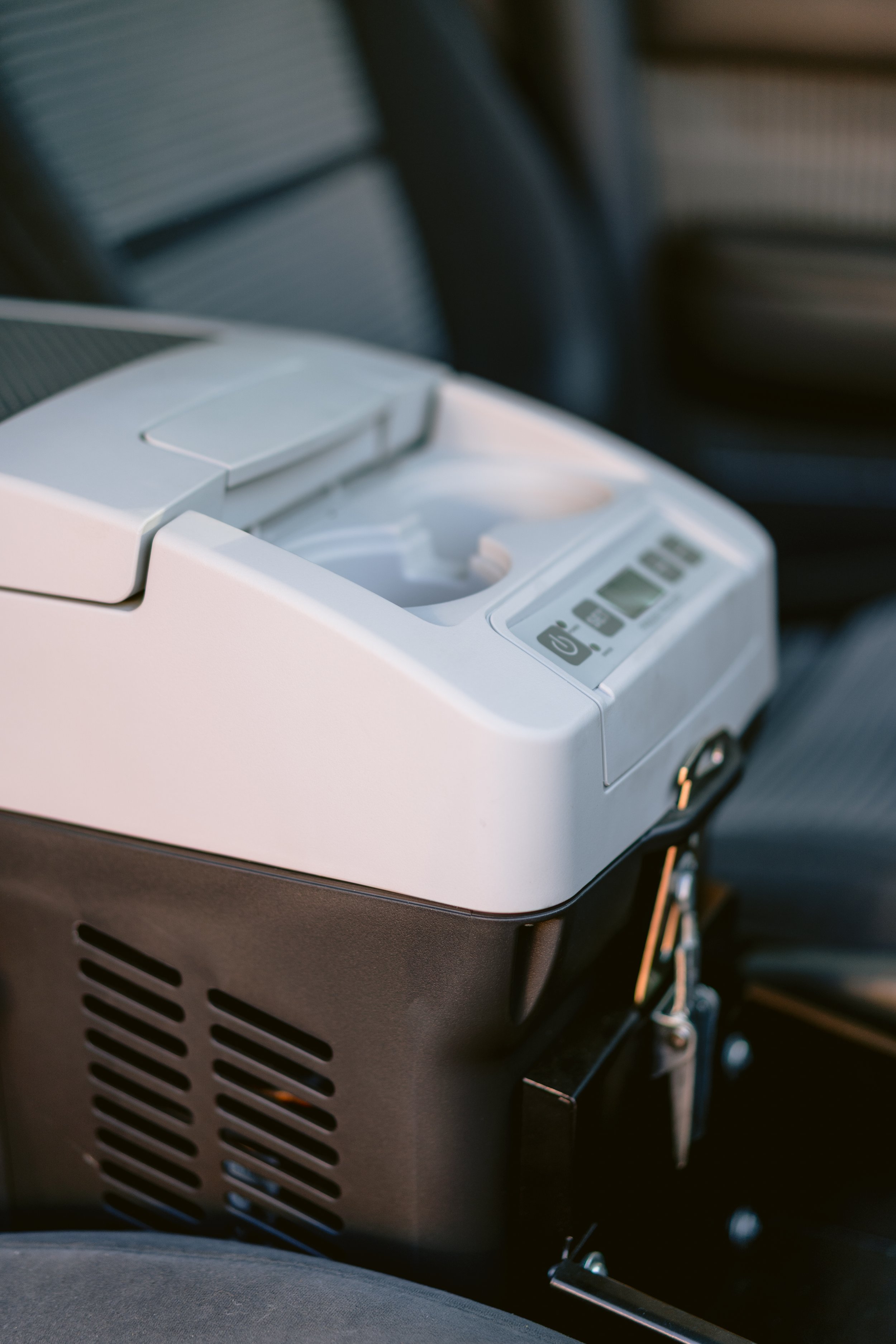 Close-up of a portable cooler with digital controls in a vehicle, with blurred vehicle interior background.