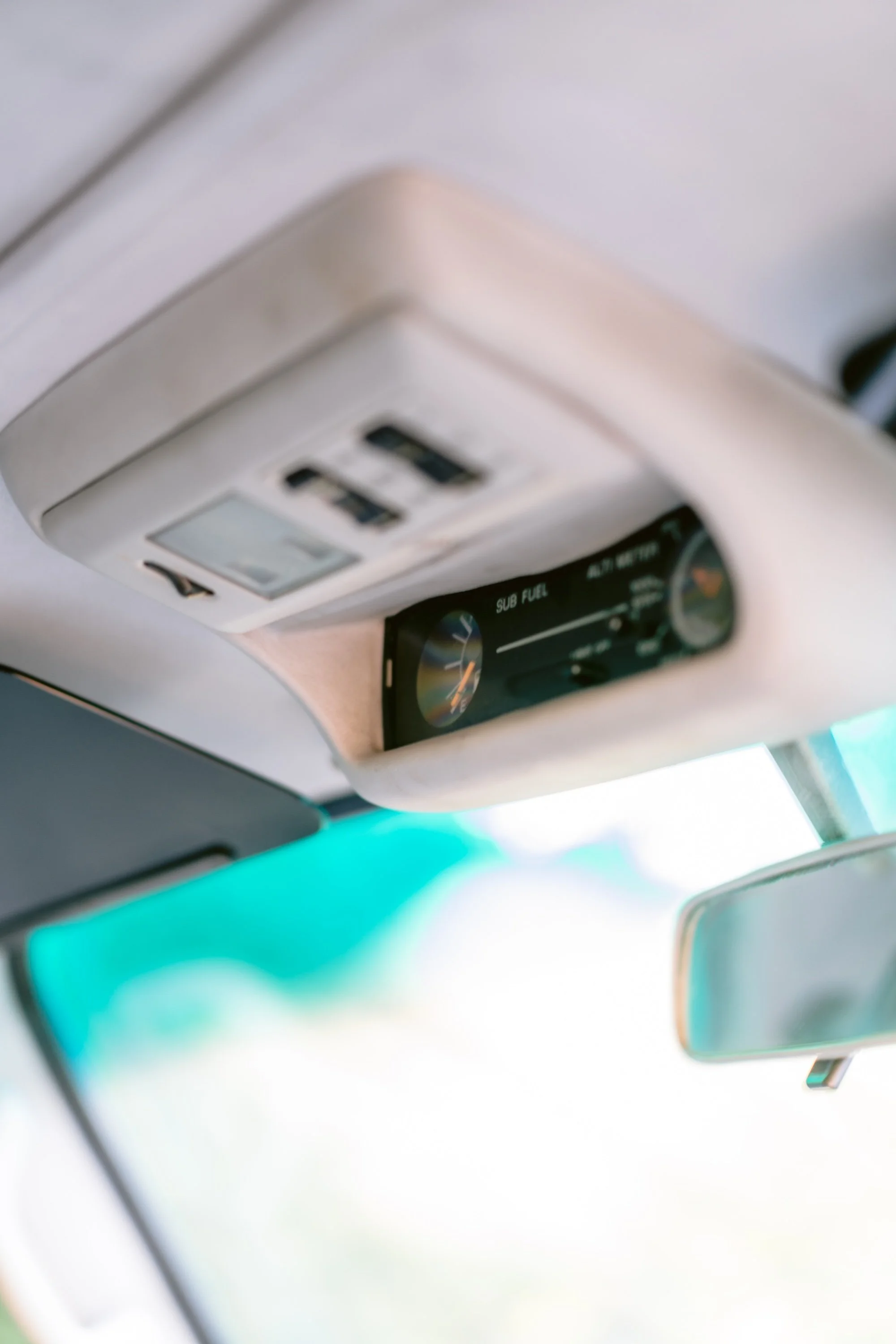 Close-up of the overhead console of a vehicle, showing a digital display and vent, with part of the rearview mirror and windshield visible.