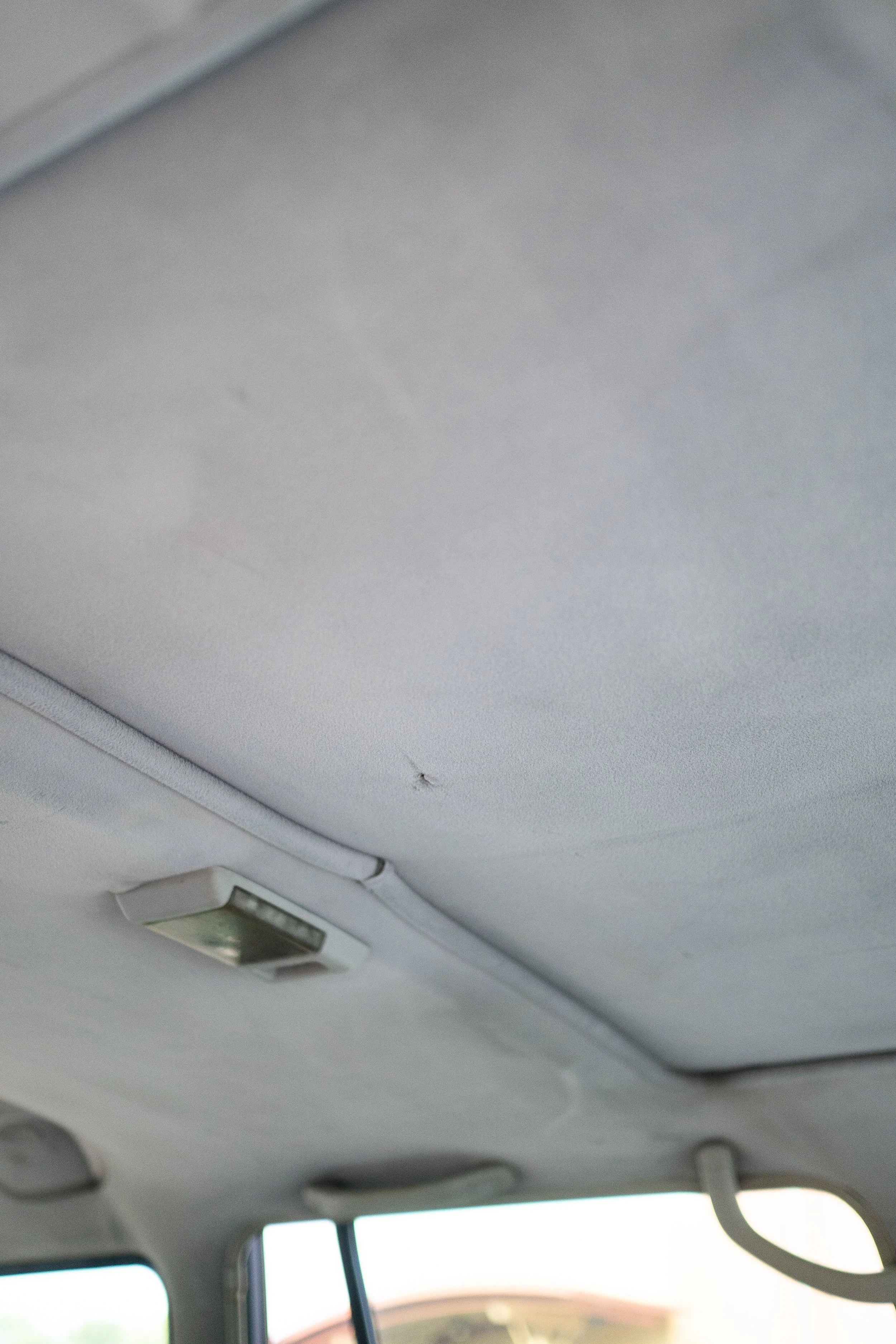 The interior roof of a vehicle shows a small ceiling light and a sunroof or moonroof with a closed cover, with parts of the vehicle window and ceiling visible.