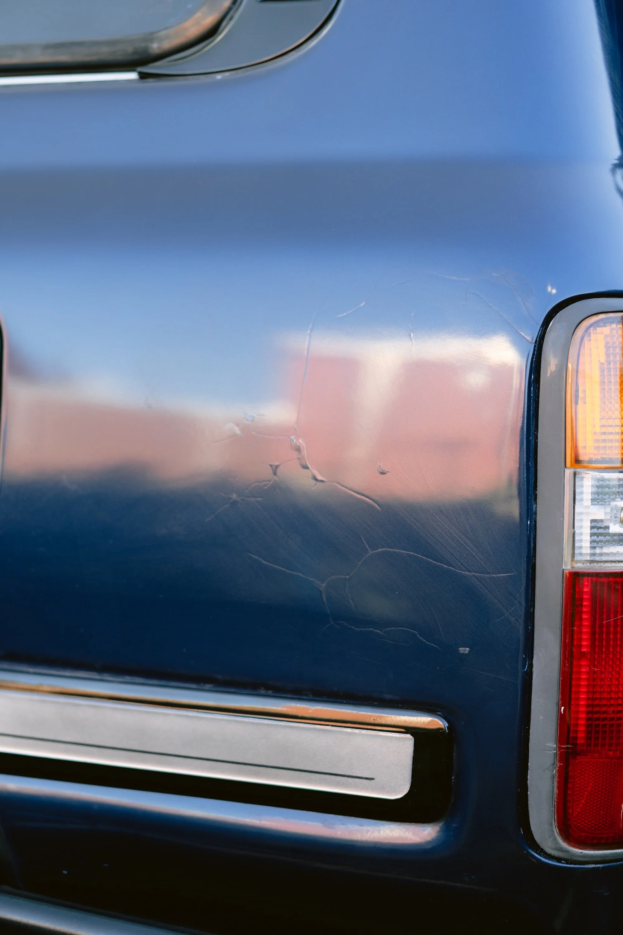 Close-up of the back of a blue vehicle showing the tail light and a scratched paint surface.