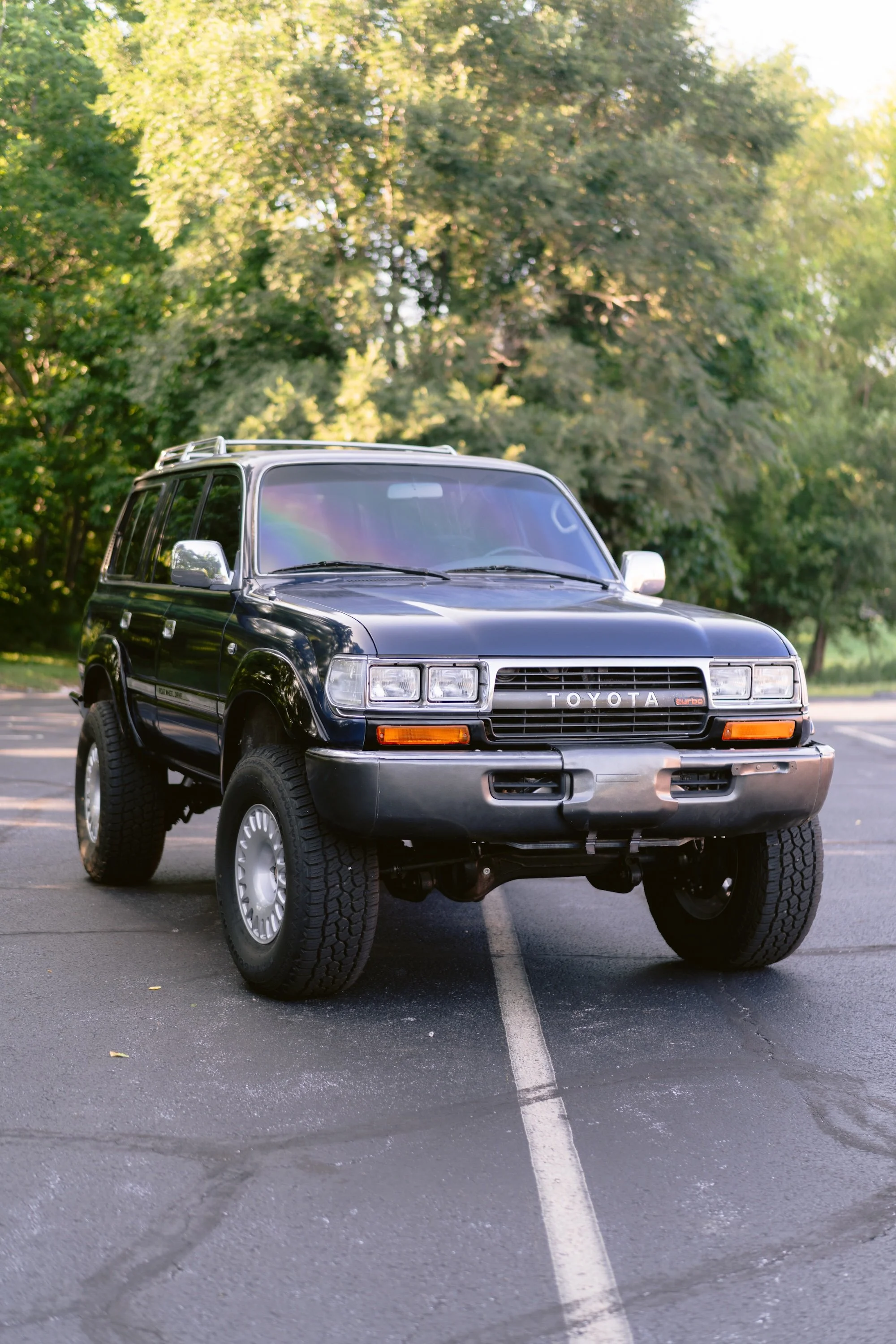 A black Toyota SUV parked in a parking lot with trees and greenery in the background.