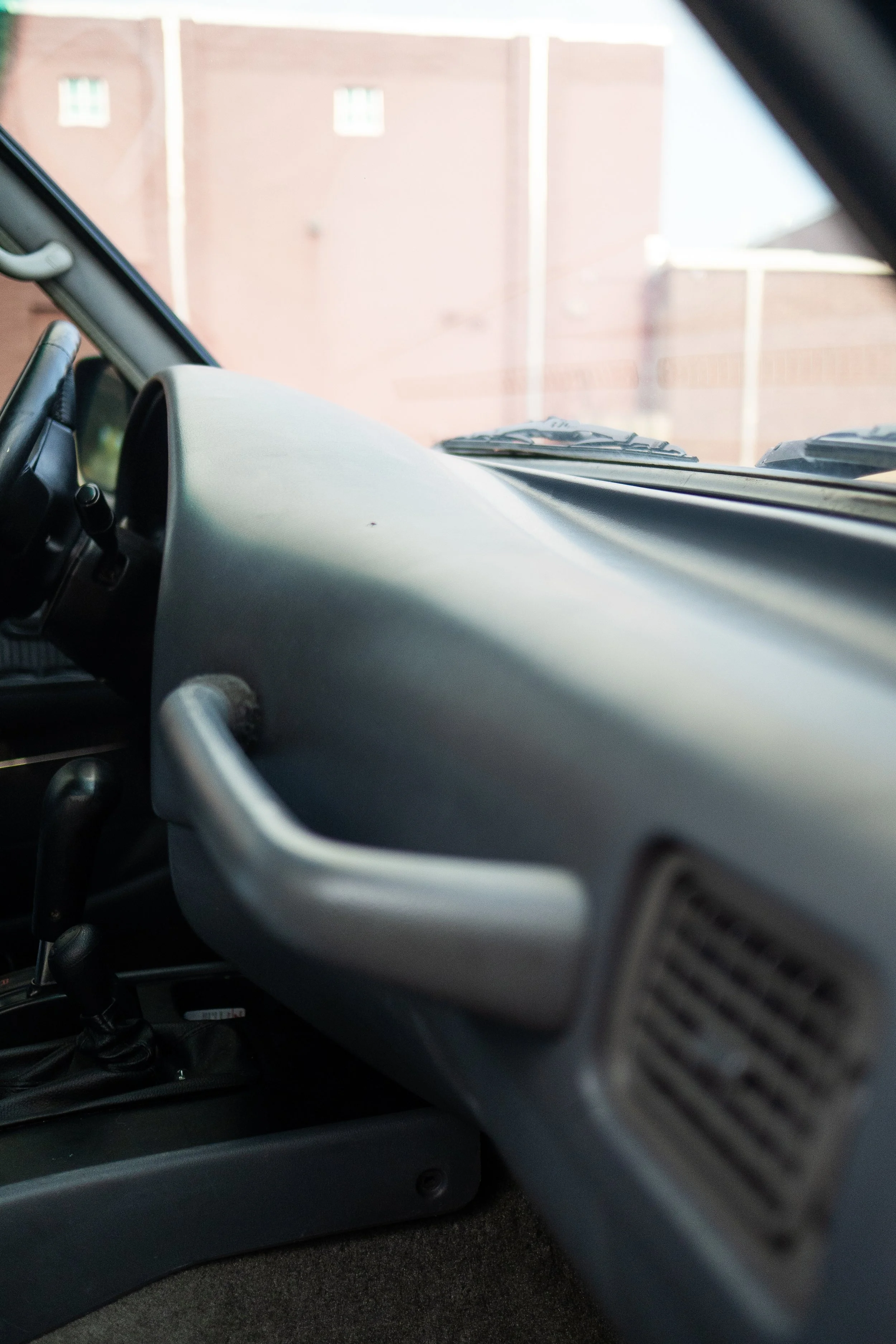 Inside view of a vehicle showing the dashboard, steering wheel, and a portion of the windshield with a brick wall outside.
