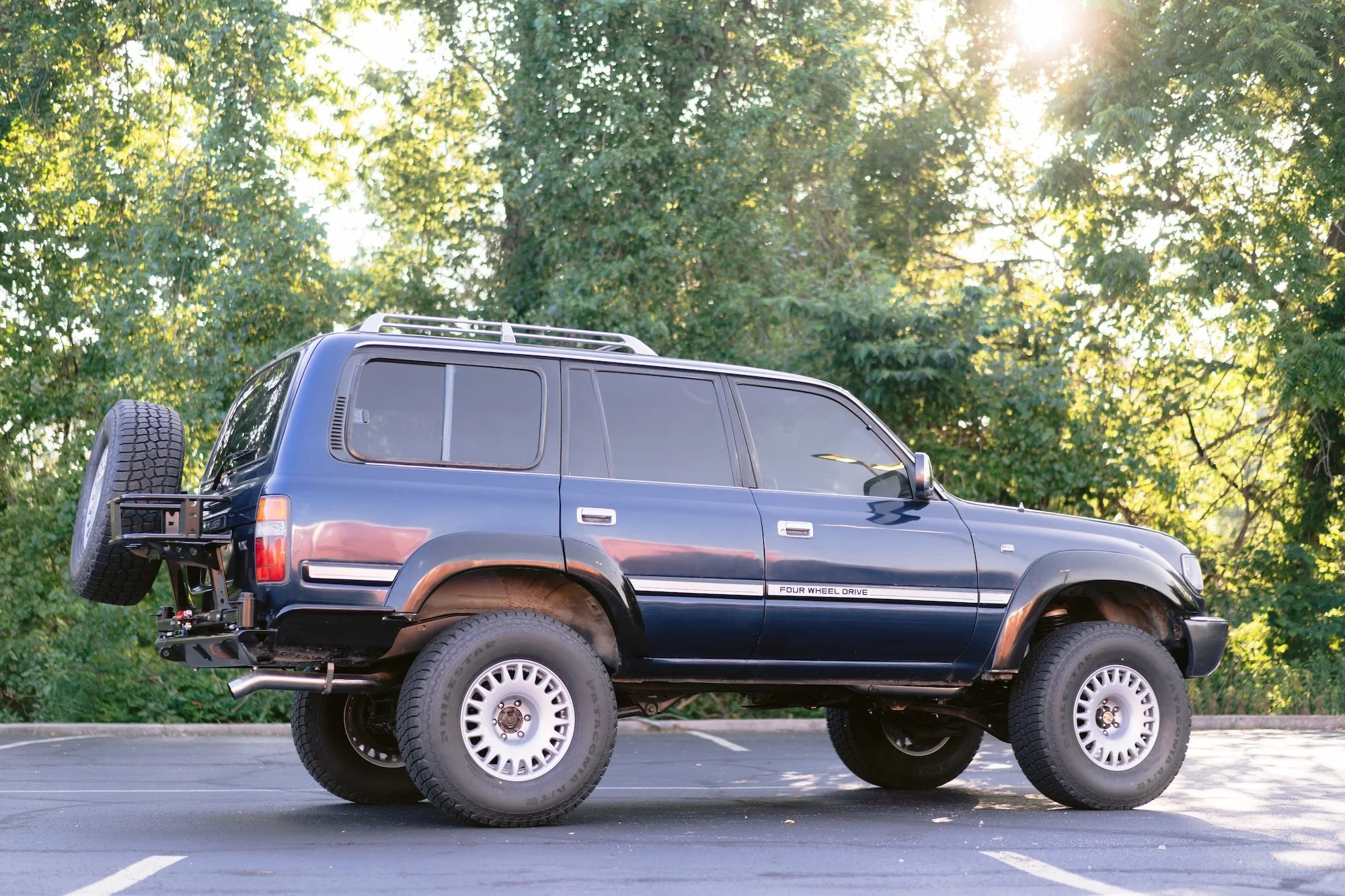 Black SUV parked on a paved lot with trees and sunlight in the background.