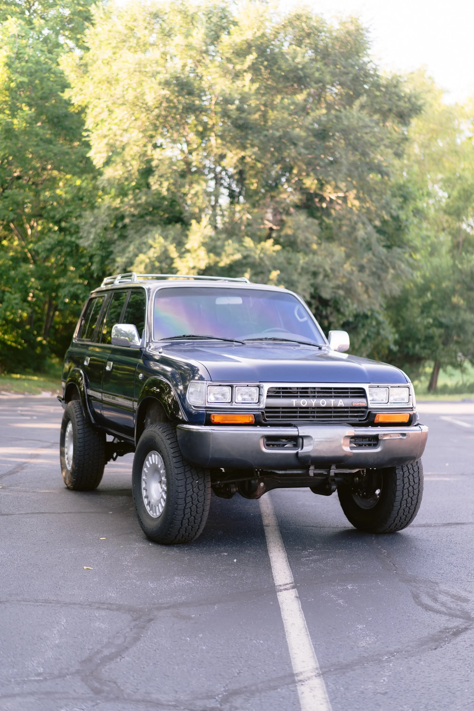 Black Toyota SUV parked in an empty parking lot with trees in the background.
