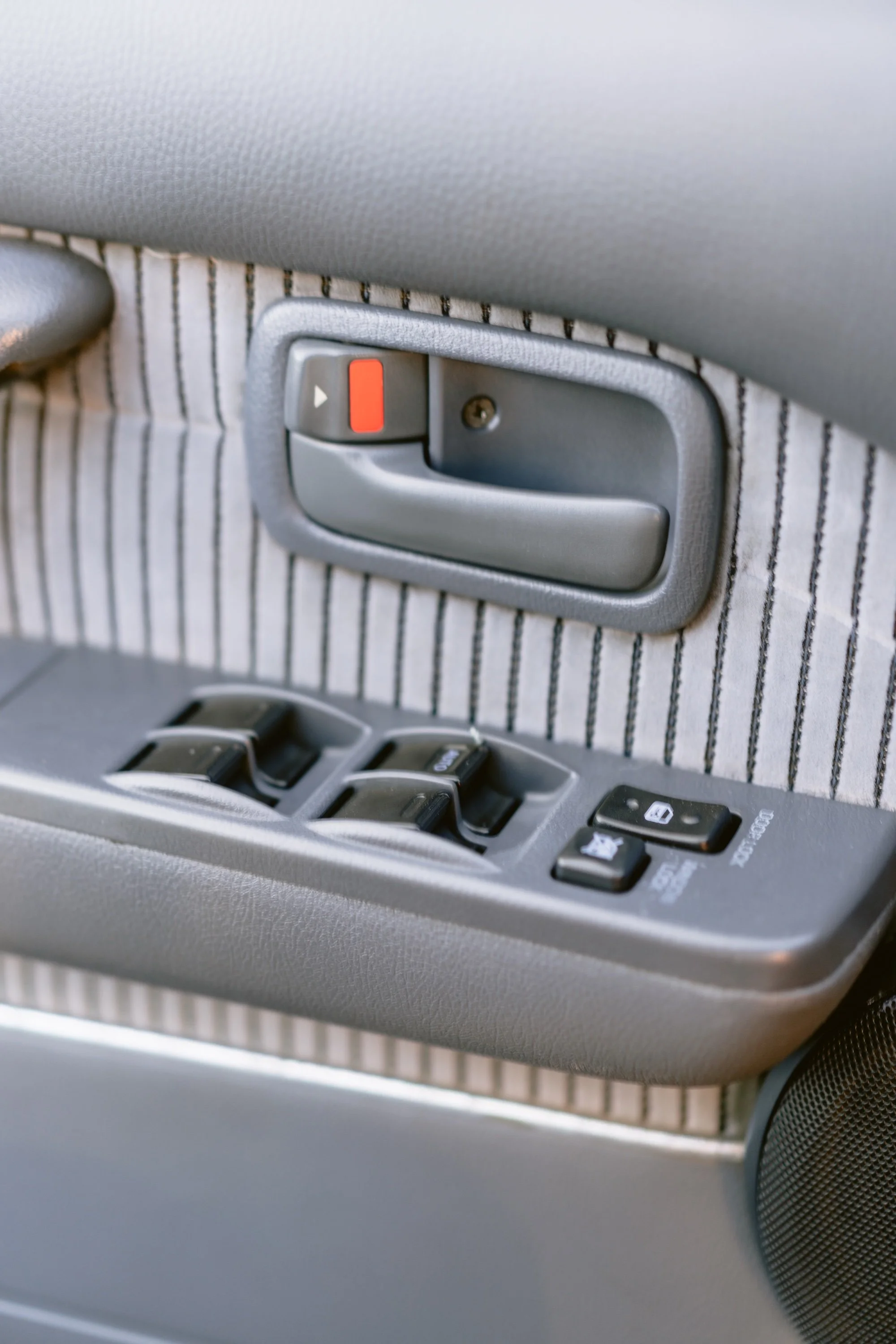 Close-up of a car's interior door panel showing the window control buttons, lock/unlock switch, and speaker grille.