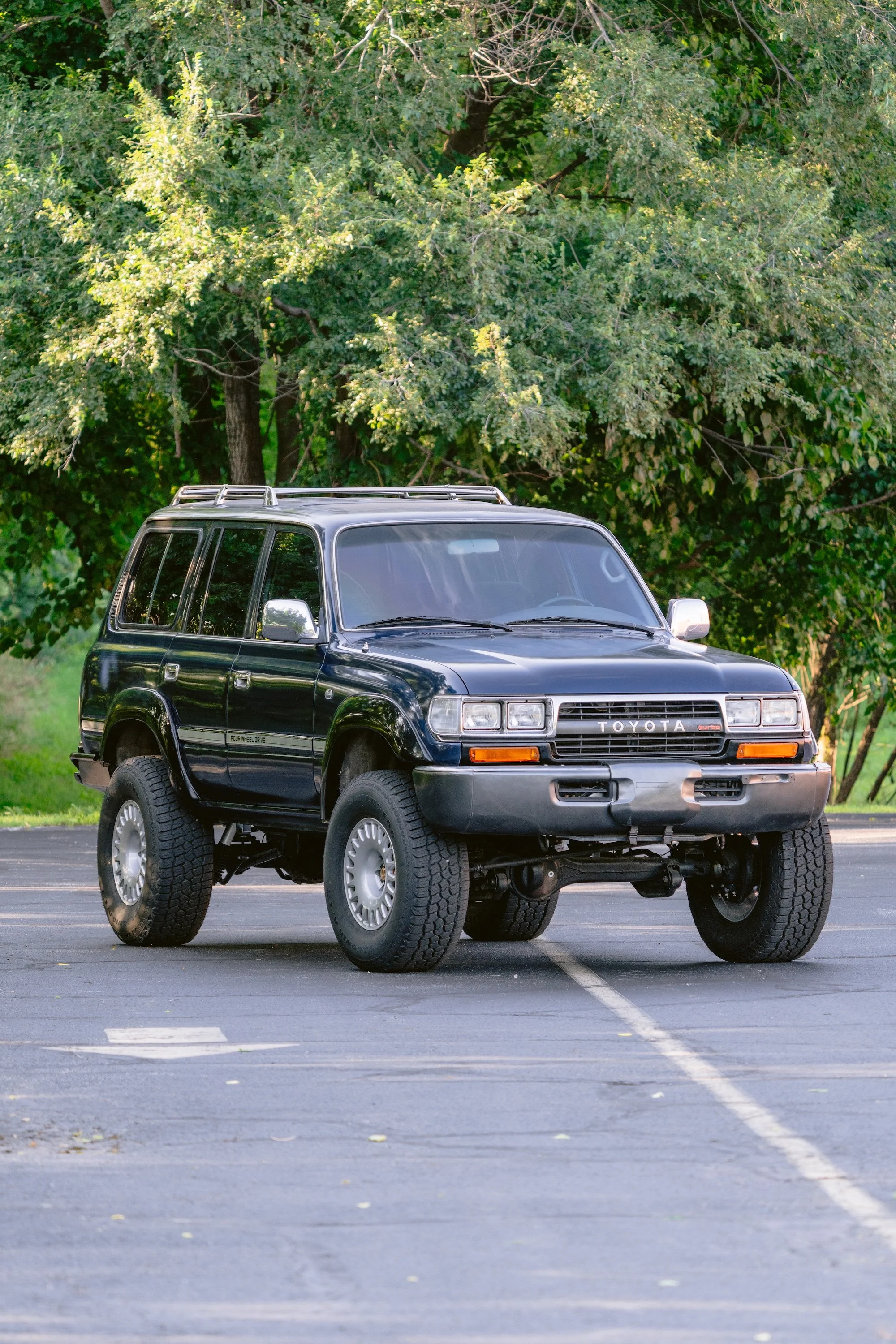 A black Toyota SUV parked in an empty parking lot with trees in the background.