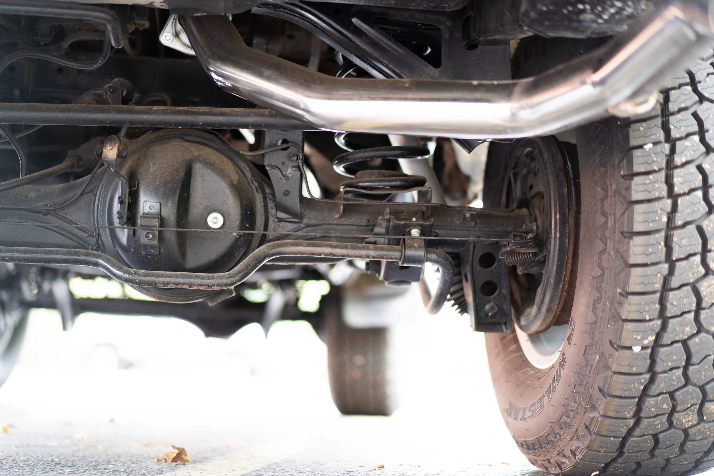 Underneath view of a truck showing its suspension system, differential, and a tire with rugged tread.