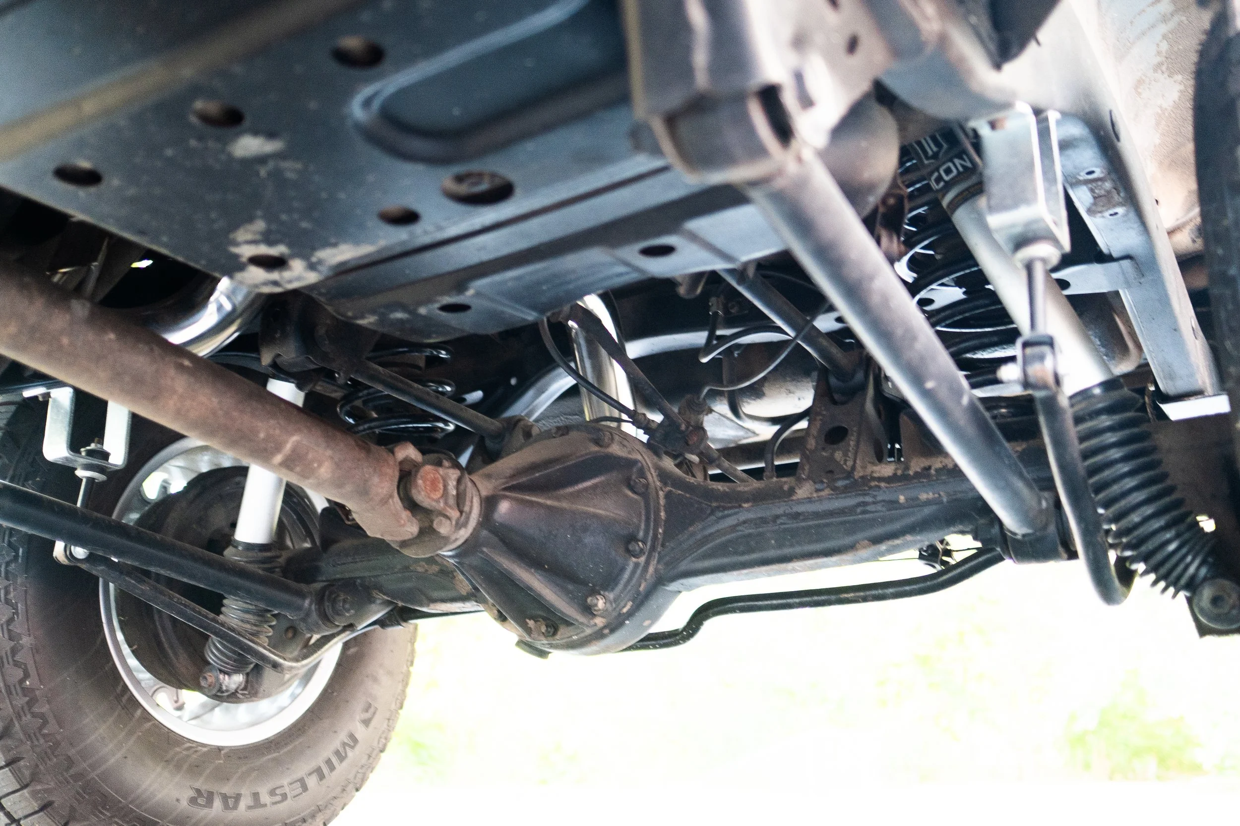 Underneath view of a vehicle's suspension system including coil springs, shock absorbers, axle, and part of the tire.