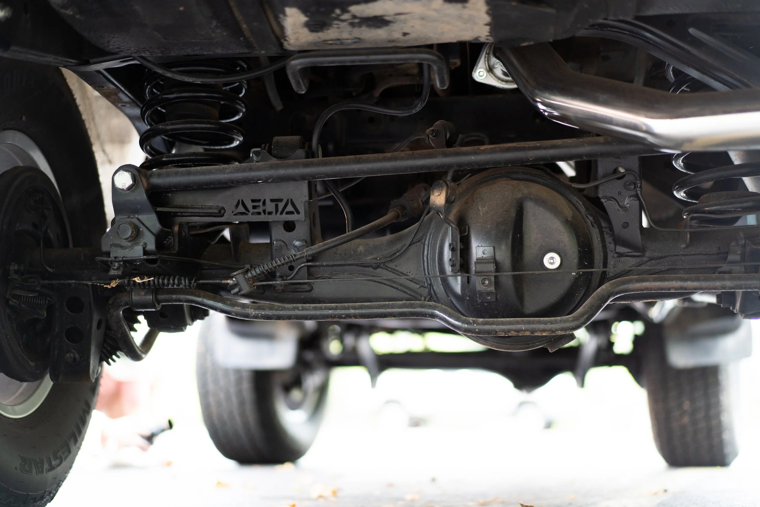 Underneath view of a car chassis showing suspension components, brake system, and drivetrain parts.