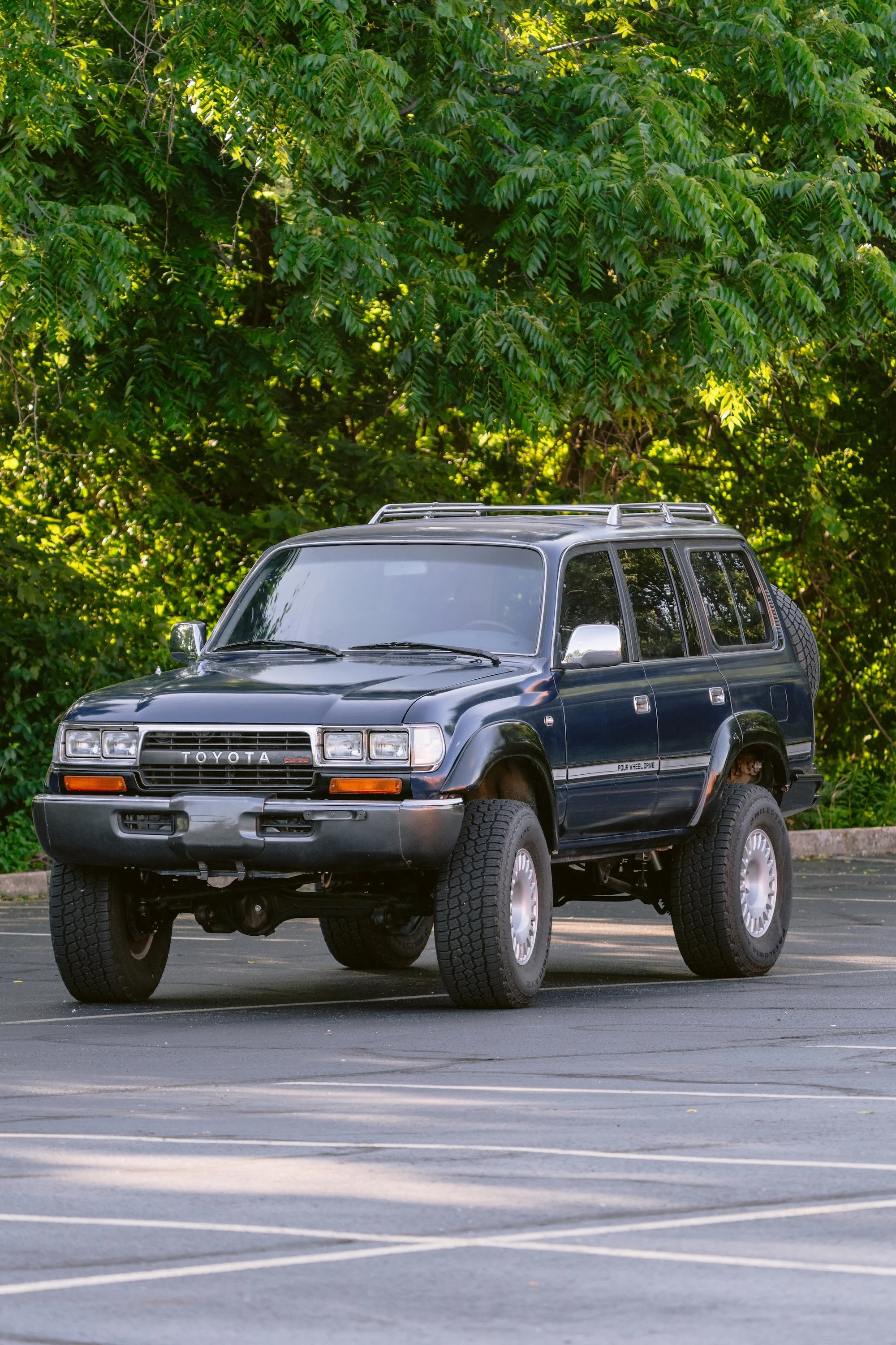 A black Toyota SUV parked in a mostly empty parking lot with green leafy trees in the background.