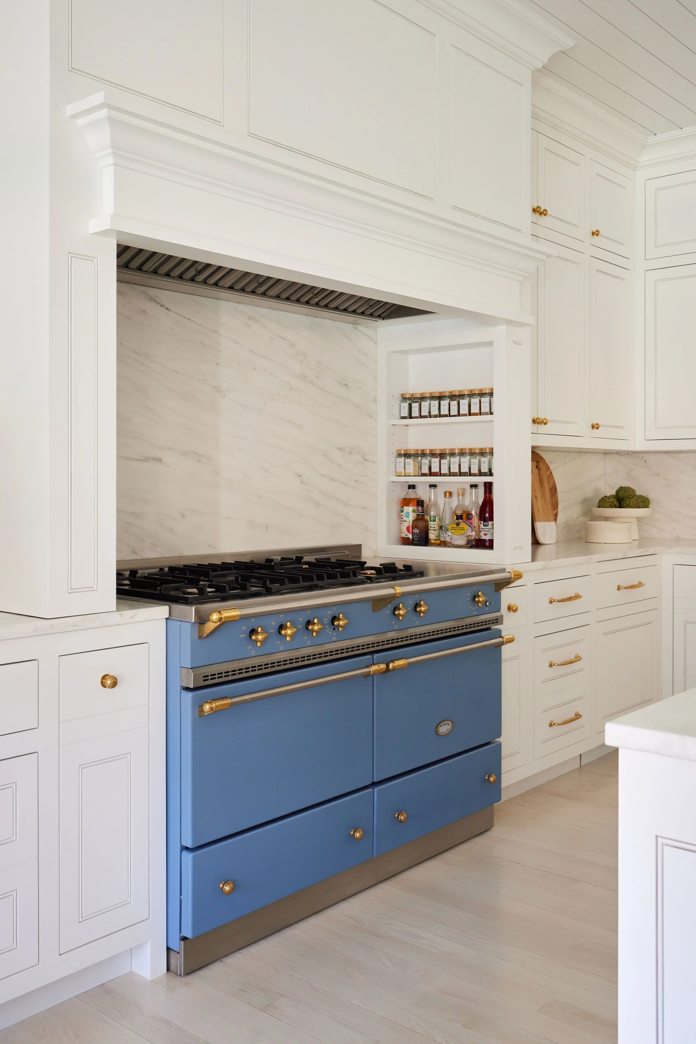 A modern kitchen with a blue stove, white cabinetry, and a marble backsplash.