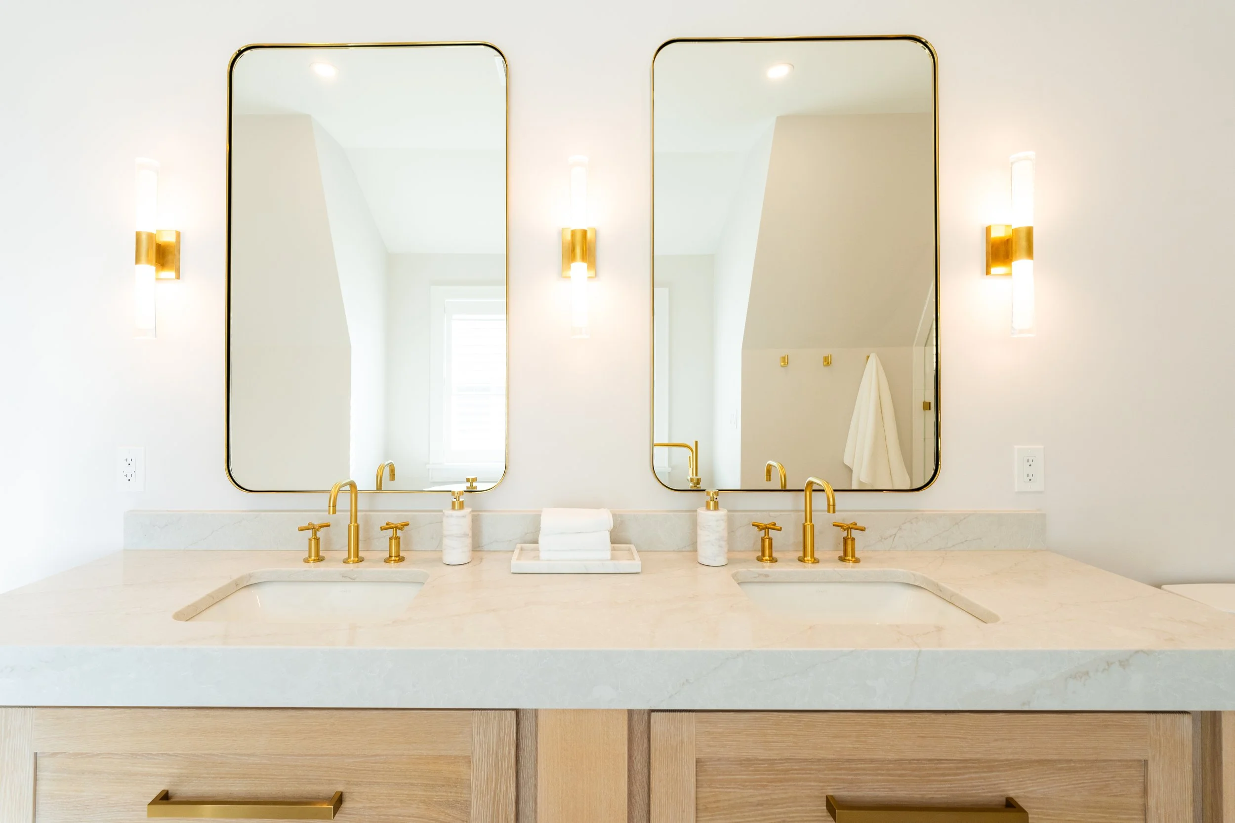 Modern bathroom vanity with double mirrors, gold fixtures, and white marble countertop, with gold and white wall lighting.