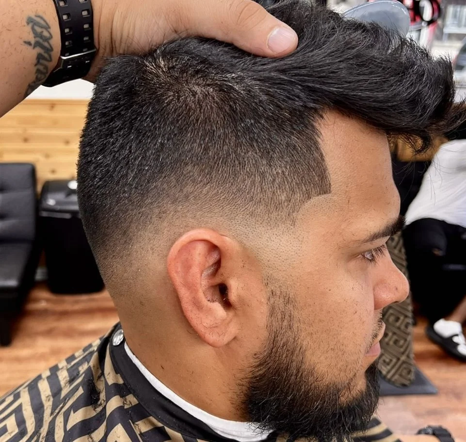 Man getting a fade haircut at a barbershop, with a hand on his head to lift hair.