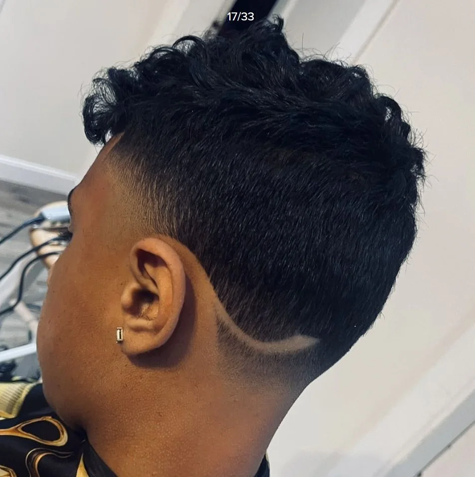 Close-up of a man's head showing a fade haircut with textured, curly hair on top and a shaved design along the side.