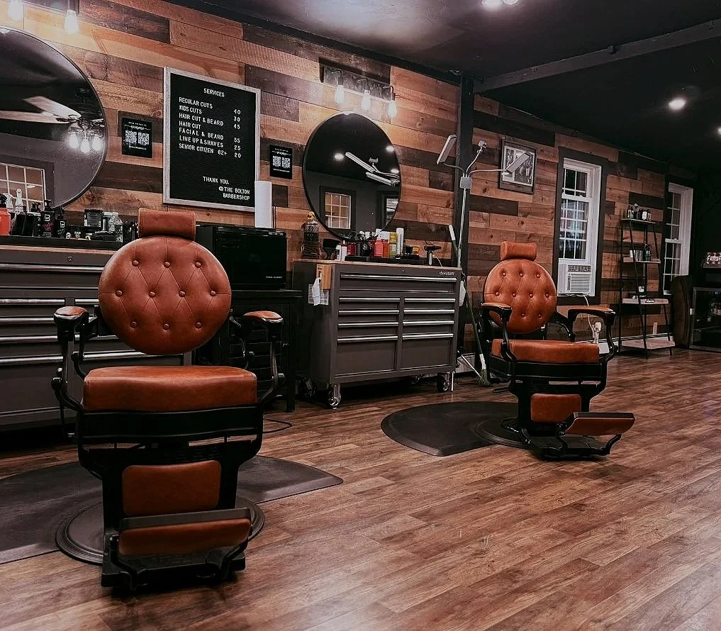 Barbershop interior with two vintage barber chairs, wooden wall decor, mirrors, a service menu, and hair styling tools.