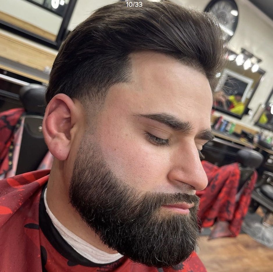 Close-up of a man with a styled haircut and full beard at a barbershop.