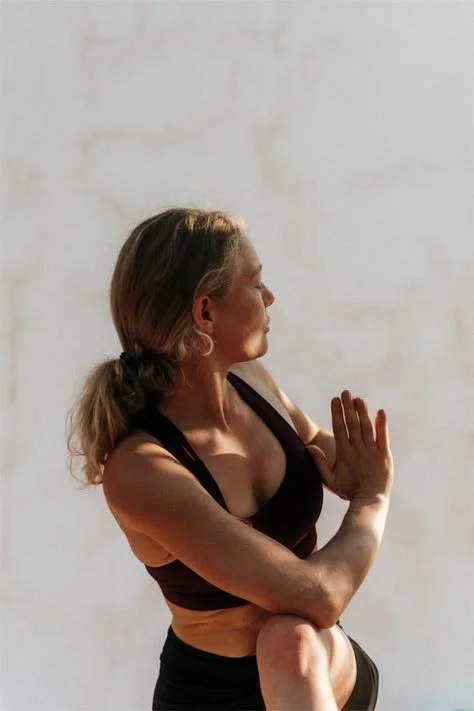 A woman practicing yoga in a meditative pose with her hands together near her chest and her eyes closed.
