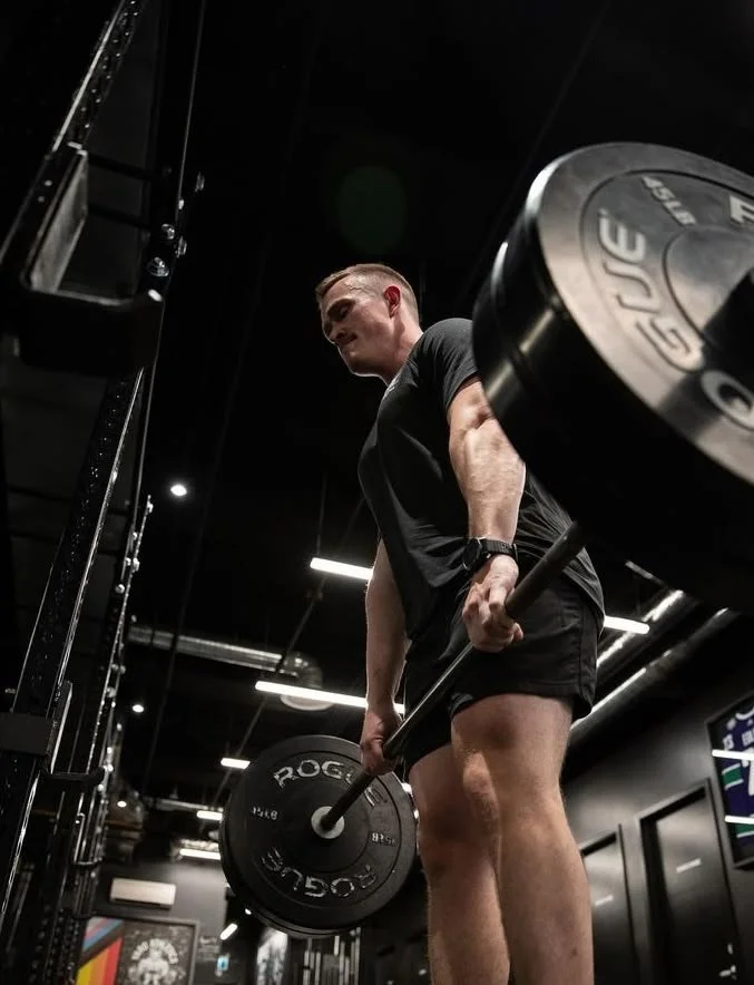A man lifting a barbell with weights in a gym, emphasizing his muscular arms and focused expression.
