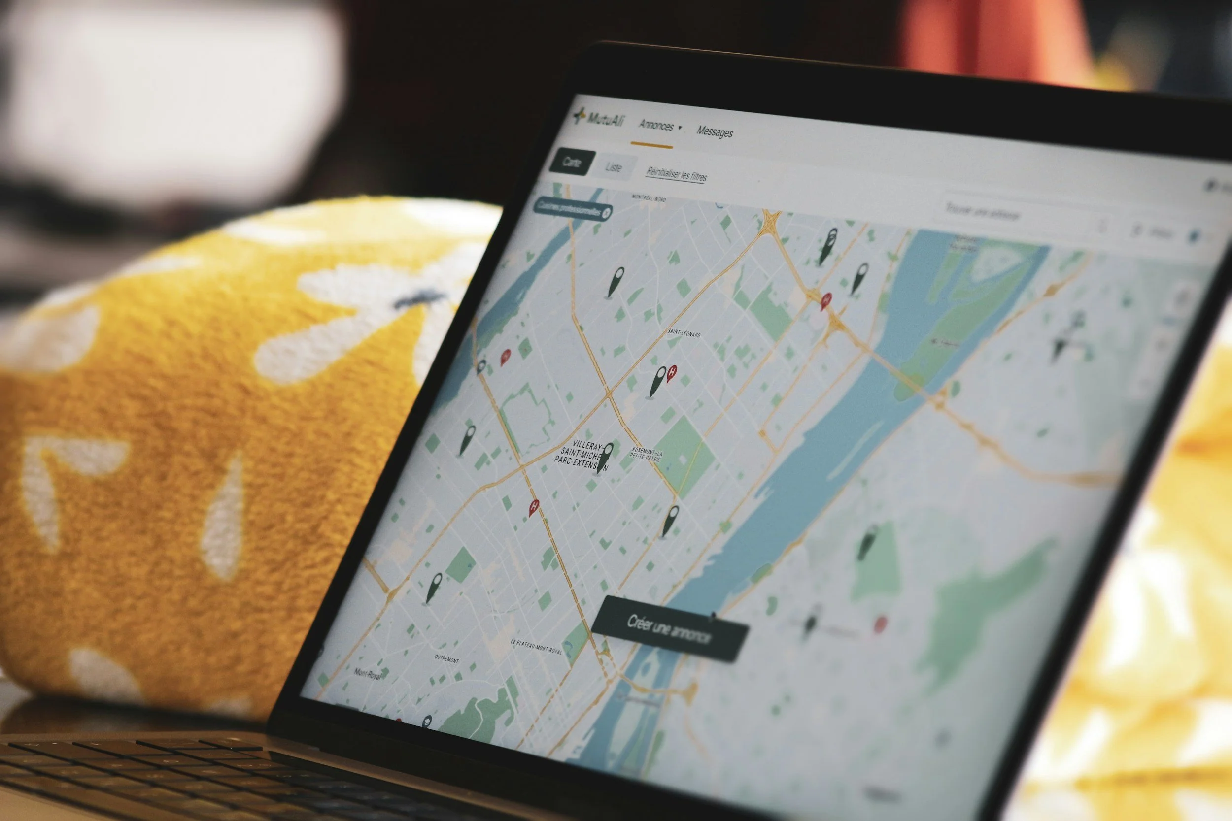 A laptop displaying a map with markers on the screen, placed on a yellow fabric surface.