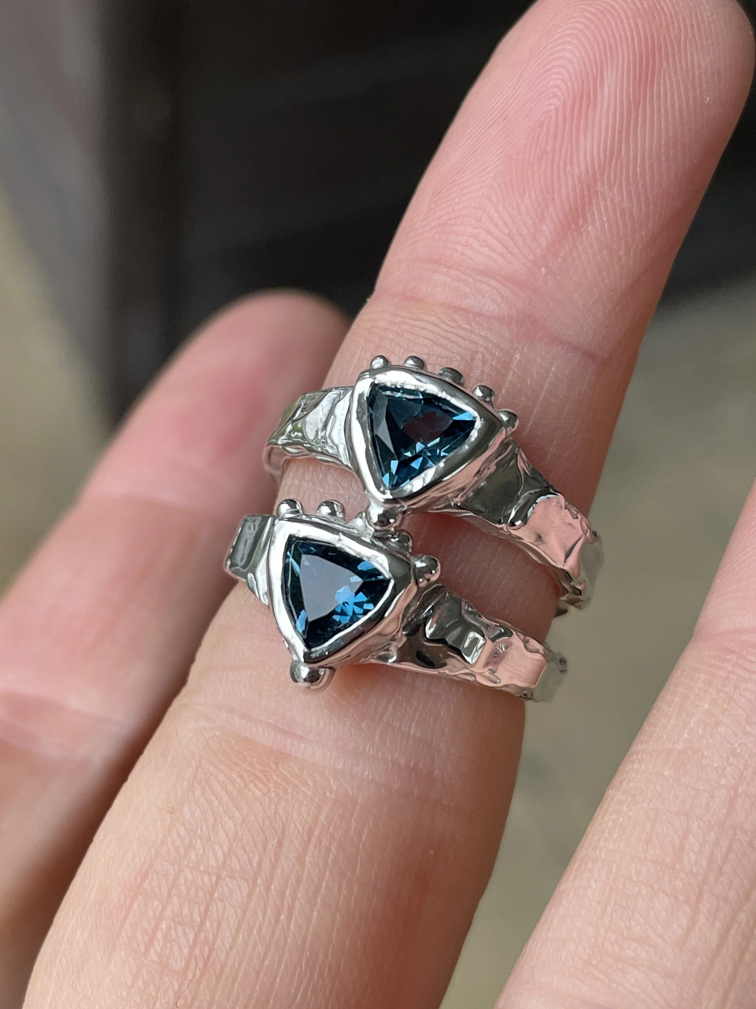 Close-up of a hand wearing a silver ring with a blue triangular gemstone.