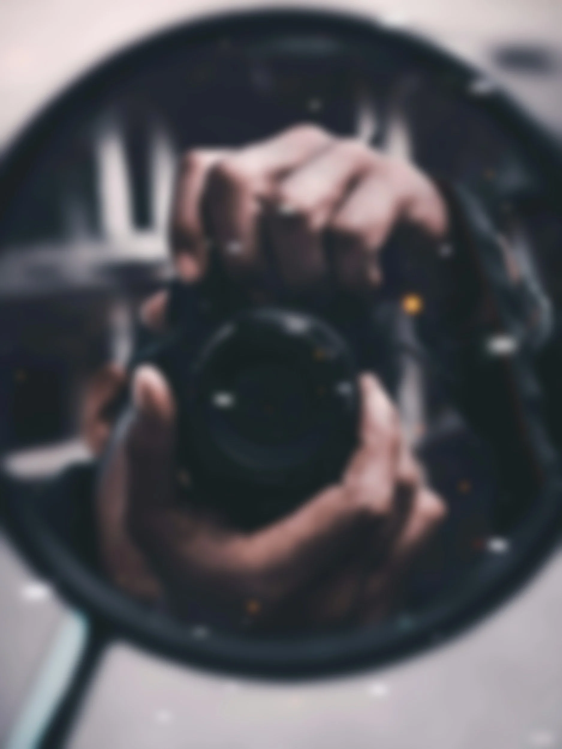 A person taking a selfie through the reflection in a shiny, metallic object, possibly a spoon or a similar utensil, with a hand holding a smartphone.