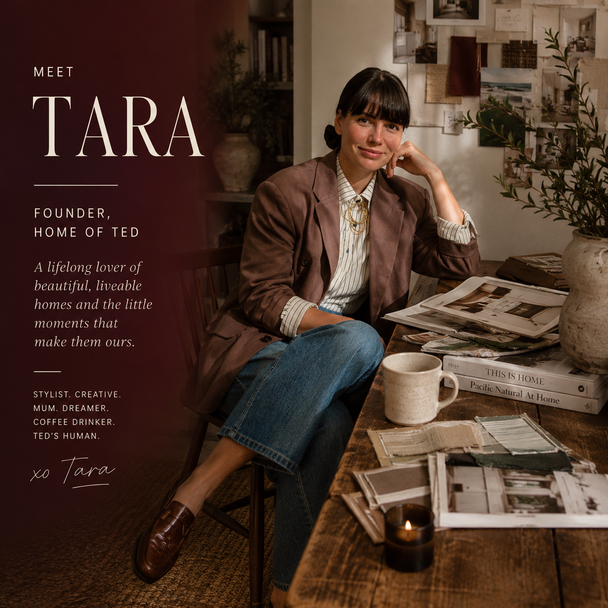 A woman sitting at a wooden table with magazines, a cup, and a candle. She wears a brown blazer, striped shirt, and jeans, smiling with her hand resting on her face. The background shows a cozy home interior with plants, books, and artwork on the wall.