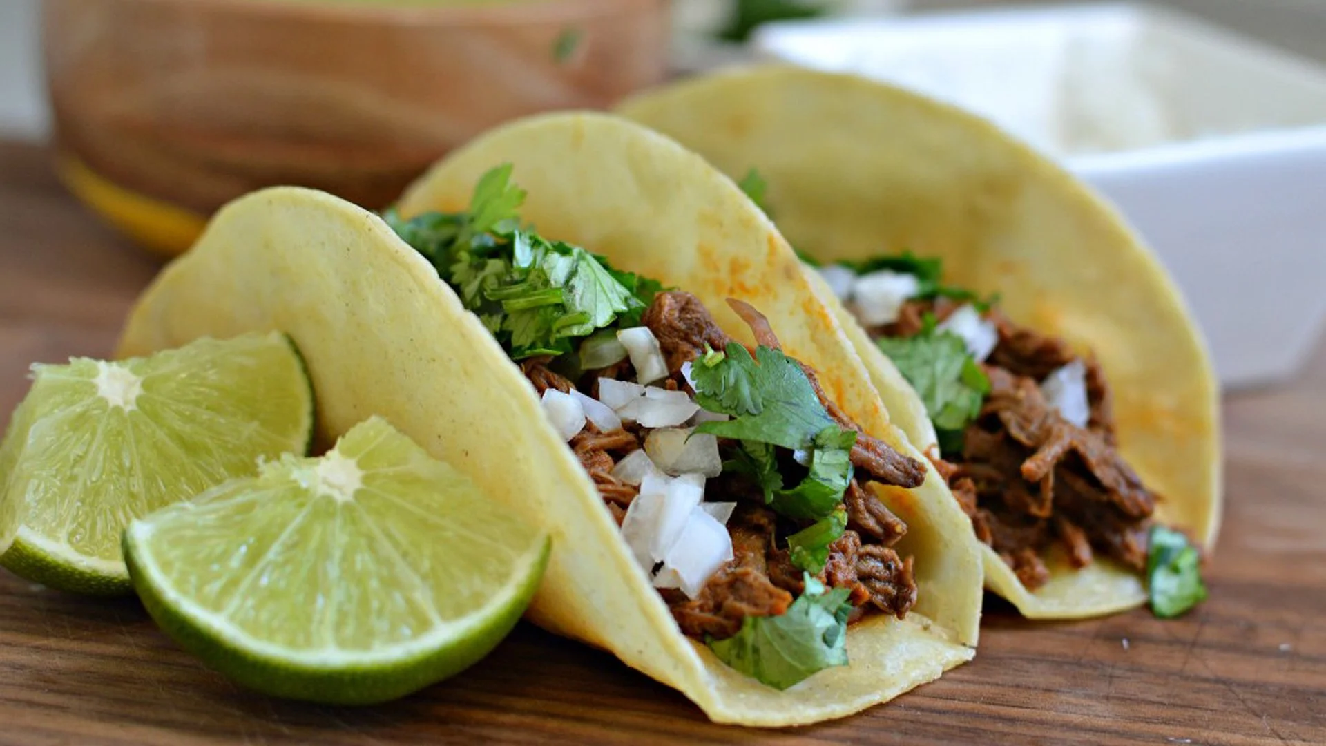 Three tacos filled with shredded meat, chopped onions, and cilantro, served with lime wedges.
