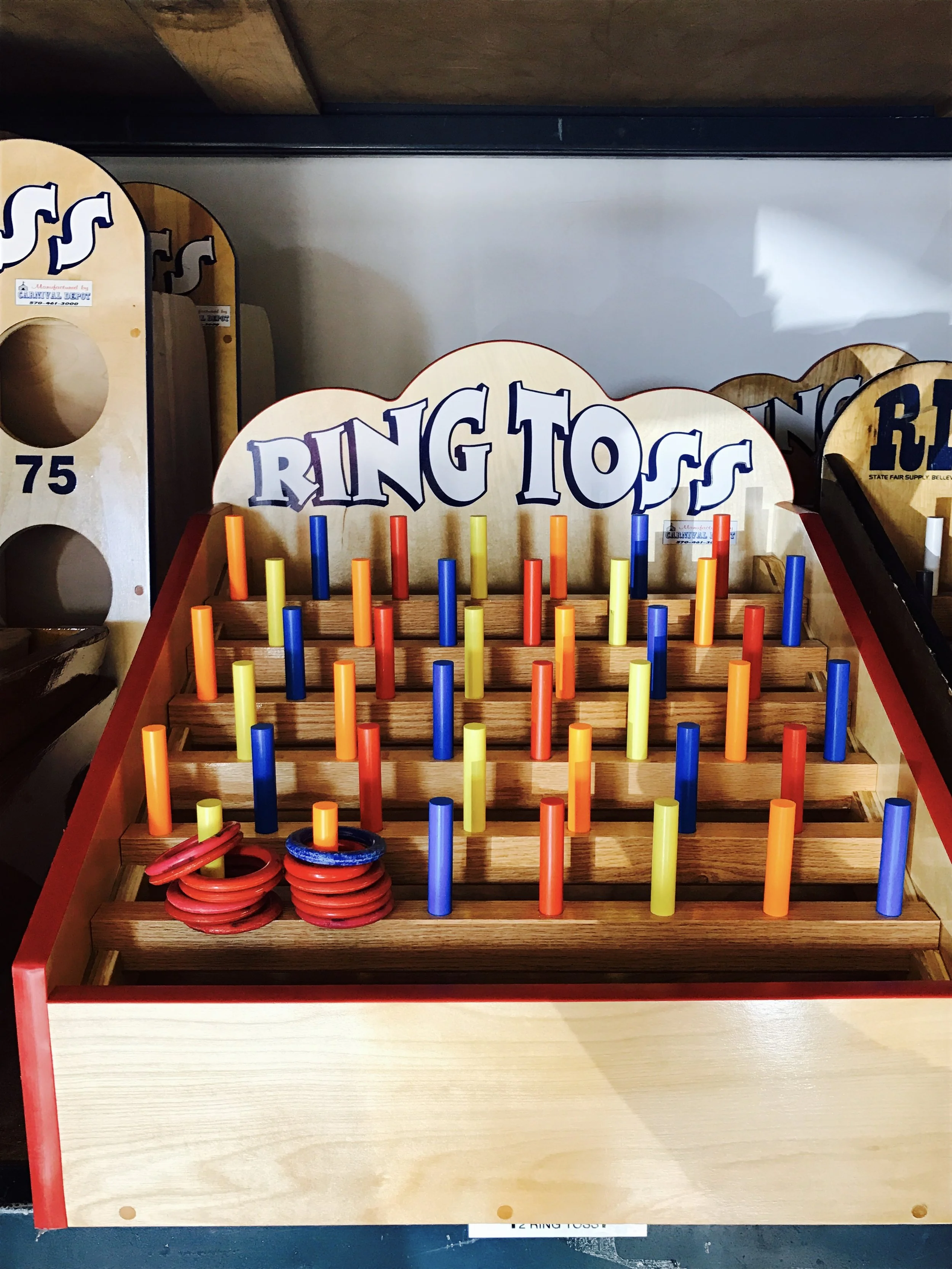 A wooden ring toss game with colored plastic pegs arranged on a display board, with rings placed on the bottom left side of the game.