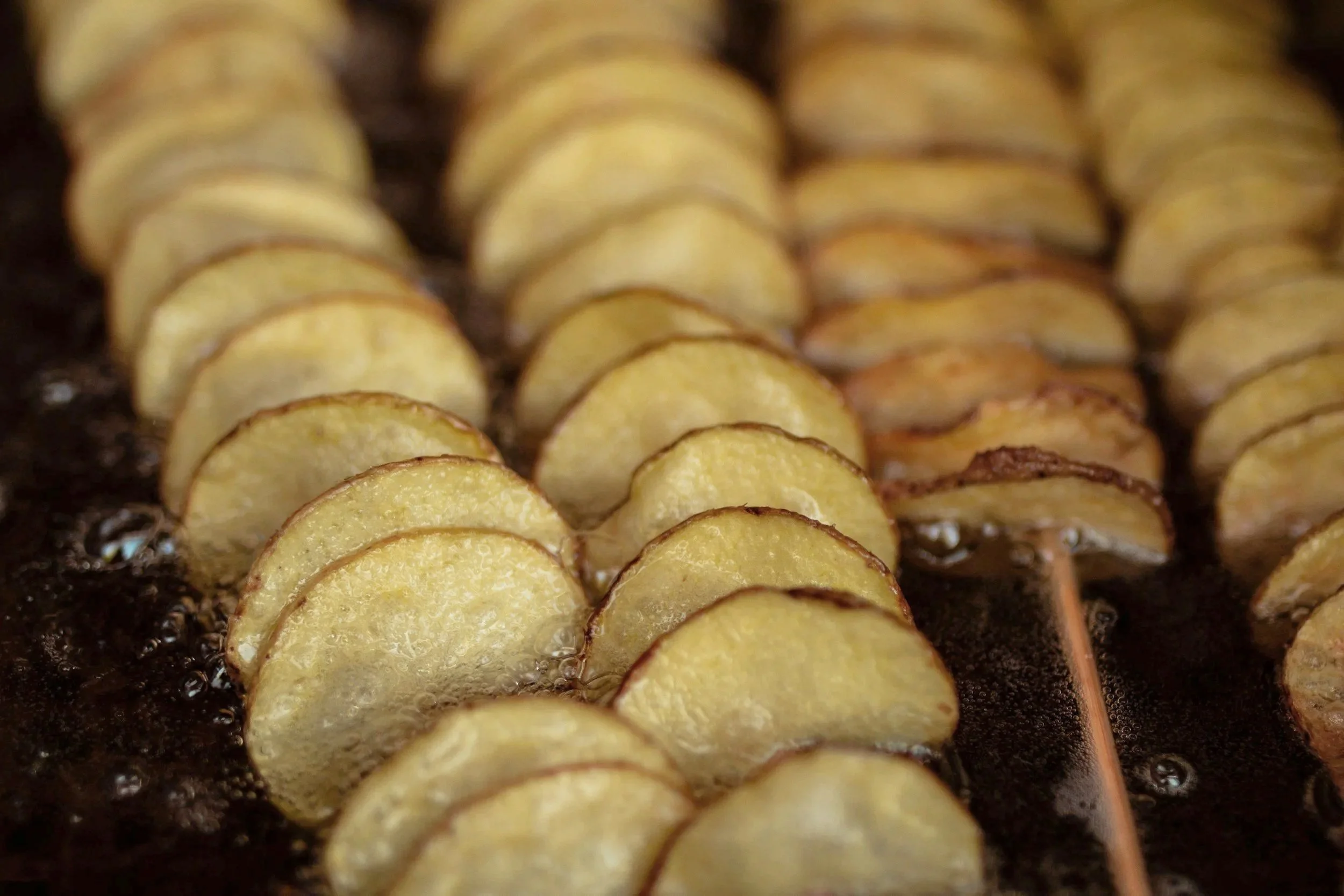 Close-up of sliced potatoes being cooked on a grill or pan with bubbling oil.