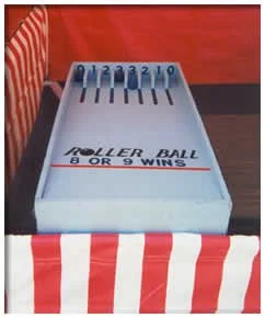 A small box with a blue top and labeled 'ROLLER BALL 6 OR 9 WINS' contains numbered plastic balls from 1 to 10, placed inside a red and white striped container.