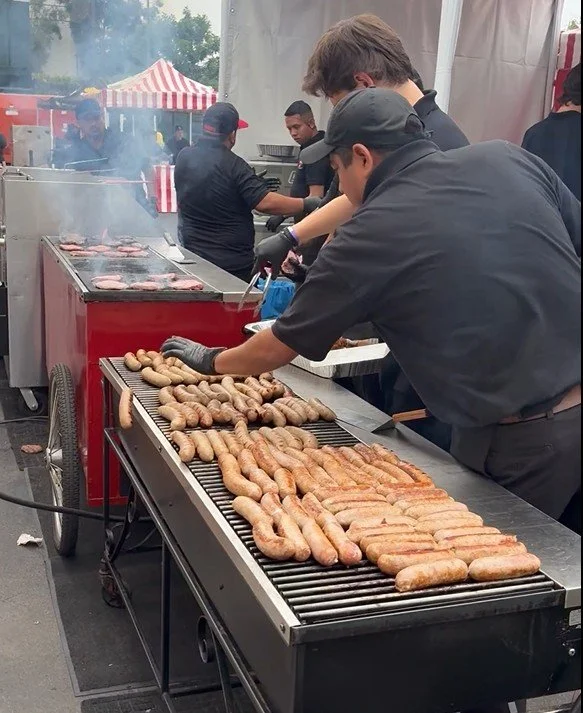 Barts Carts Staff grilling sausages on a large outdoor grill at a speical event