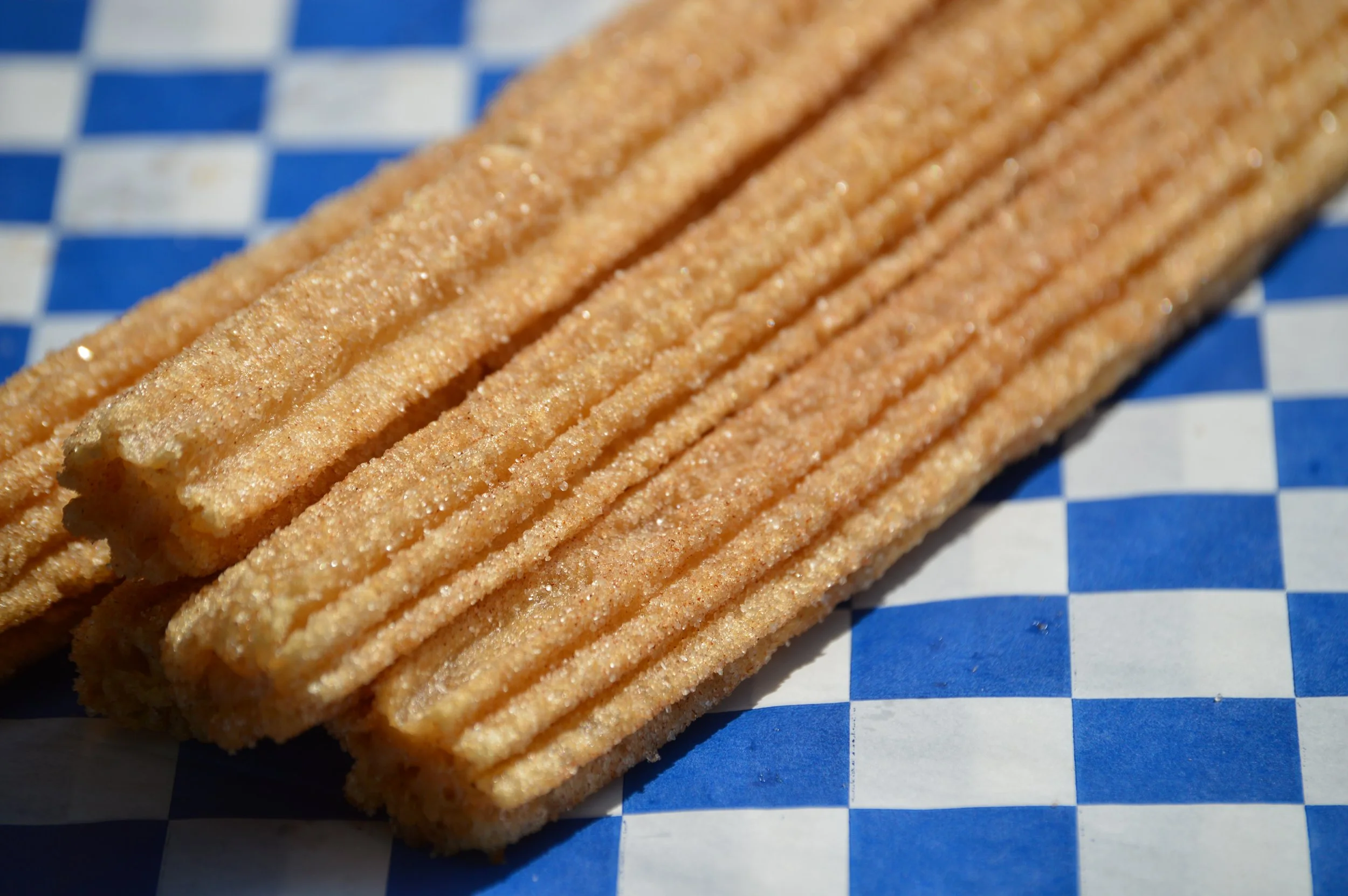 Close-up of a row of crispy, ridged potato chips on a blue and white checkered paper.