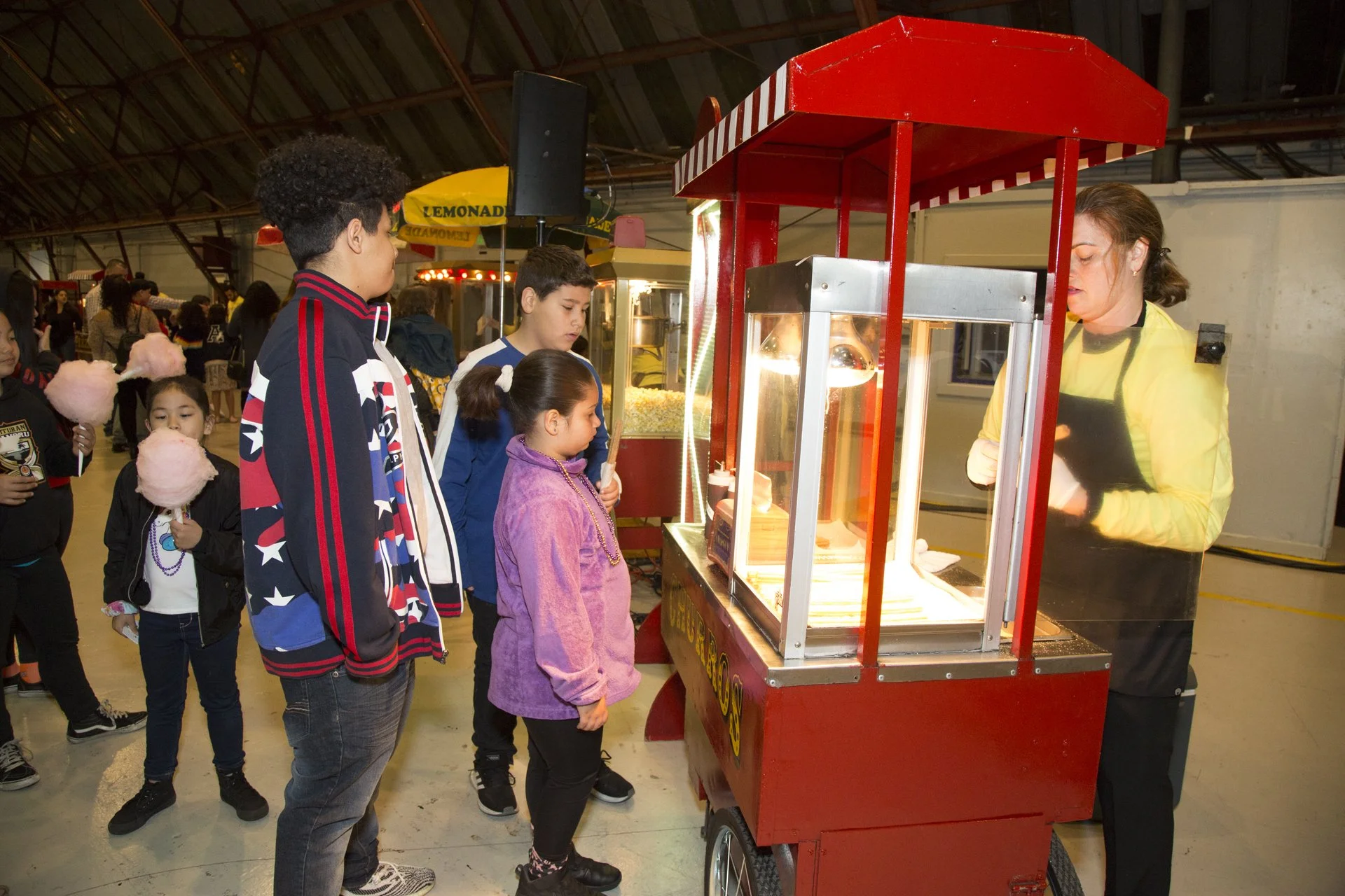 Children waiting in line at a cotton candy stand at an indoor event.