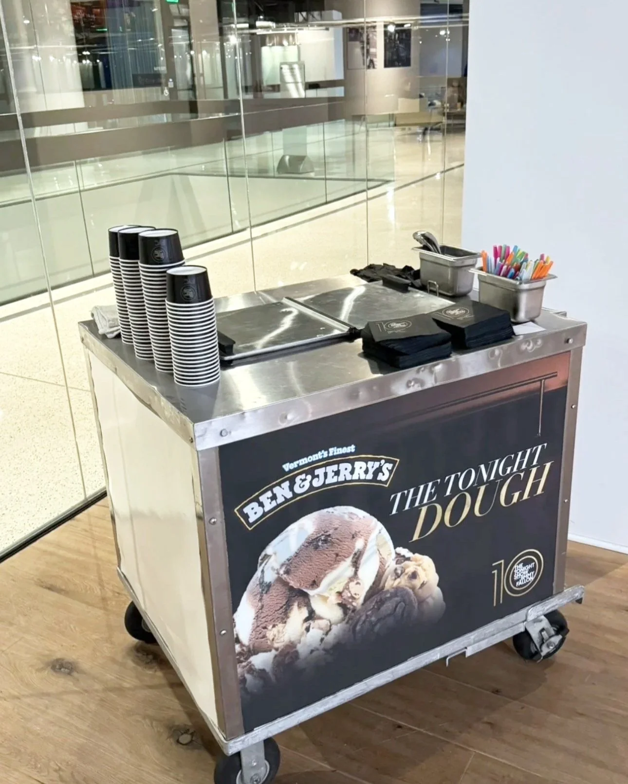 Ben & Jerry's ice cream cart in an airport or mall, with cups, napkins, and utensils on top, advertising 'The Tonight Dough' flavor.