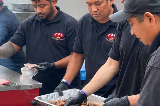 Three men wearing black shirts and gloves preparing food at a food station.