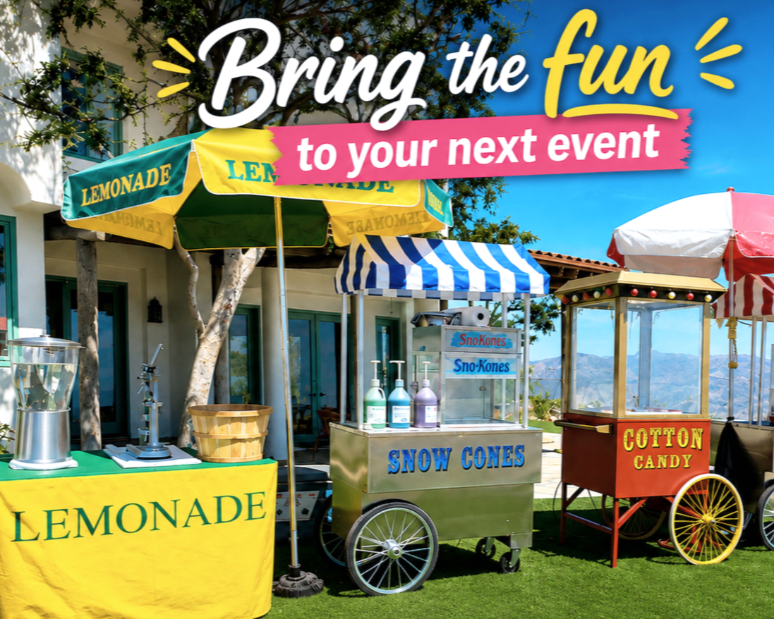 Colorful outdoor food stand with umbrellas selling lemonades, snow cones, and cotton candy with a mountain view in the background.