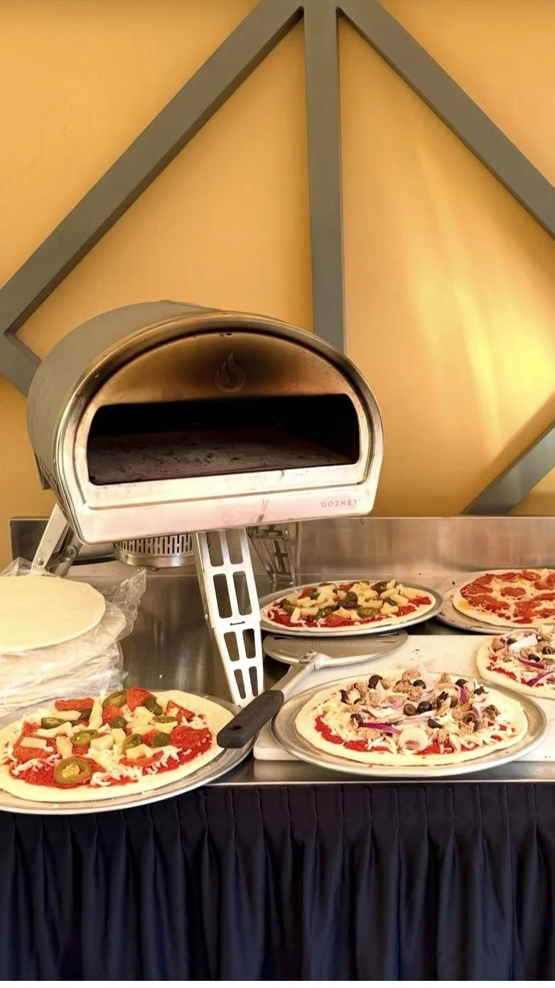 A pizza oven with multiple uncooked pizzas on plates showcasing various toppings, set against a yellow wall with geometric gray framing.
