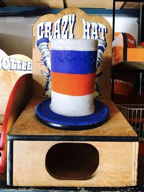 A wooden display with a painted beer mug showing the Irish flag, positioned in front of a back sign that says "Crazy Hat."