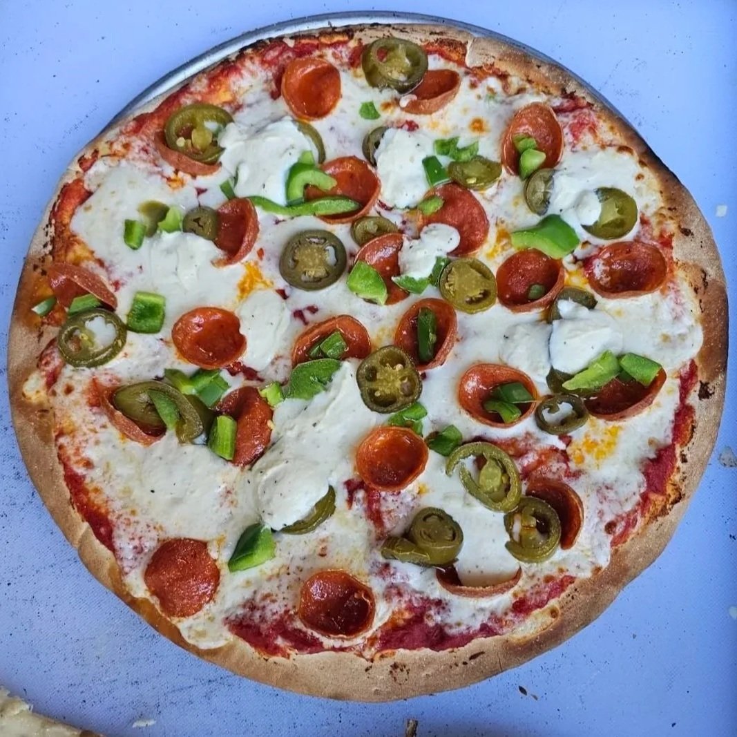 A pizza with cheese, cherry tomatoes, green onions, and jalapeño peppers on a blue surface.