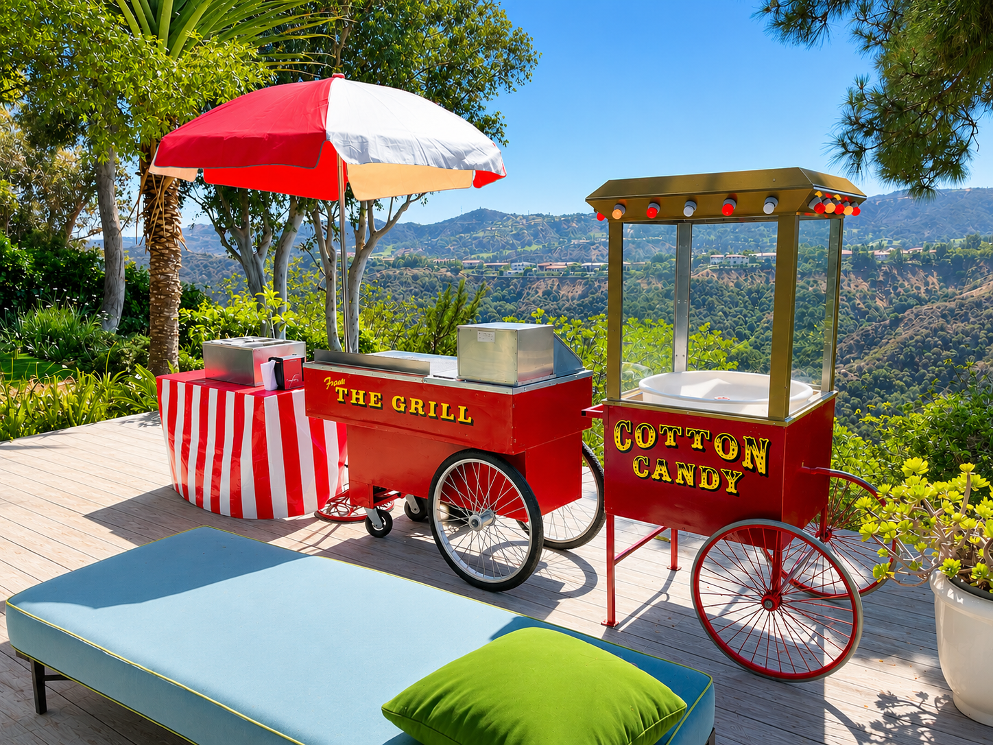 Outdoor scene with a red and white striped umbrella, red ice cream or popcorn cart labeled 'COTTON CANDY', another red cart labeled 'THE GRILL', a blue lounge chair with green pillow, and lush greenery with hills and mountains in the background.