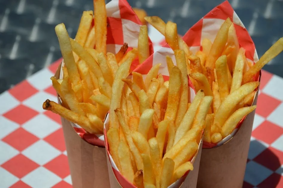 Three paper cones filled with French fries on a red and white checkered table.