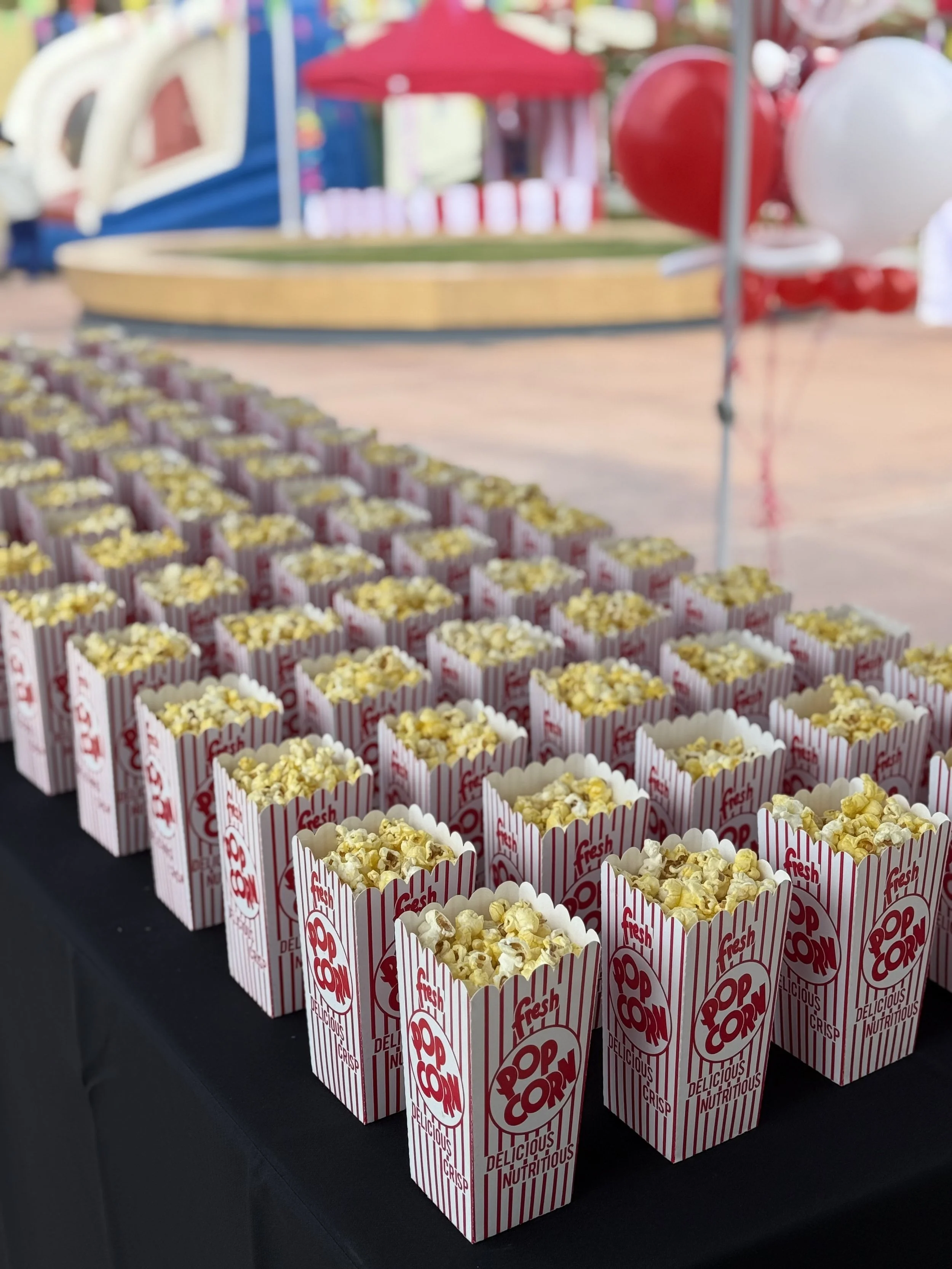 Multiple red and white striped popcorn boxes filled with popcorn placed on a black surface at a carnival or fairground.